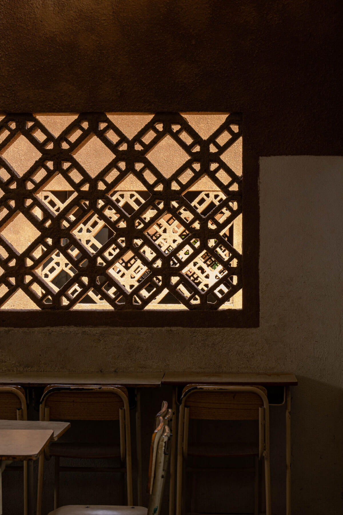 Detalhe da janela gradeada numa sala de aula, com luz suave a filtrar pelos elementos geométricos. — Escola Kapalanga arquitetura Paulo Moreira Architectures e PARQ Arquitectos em Luanda