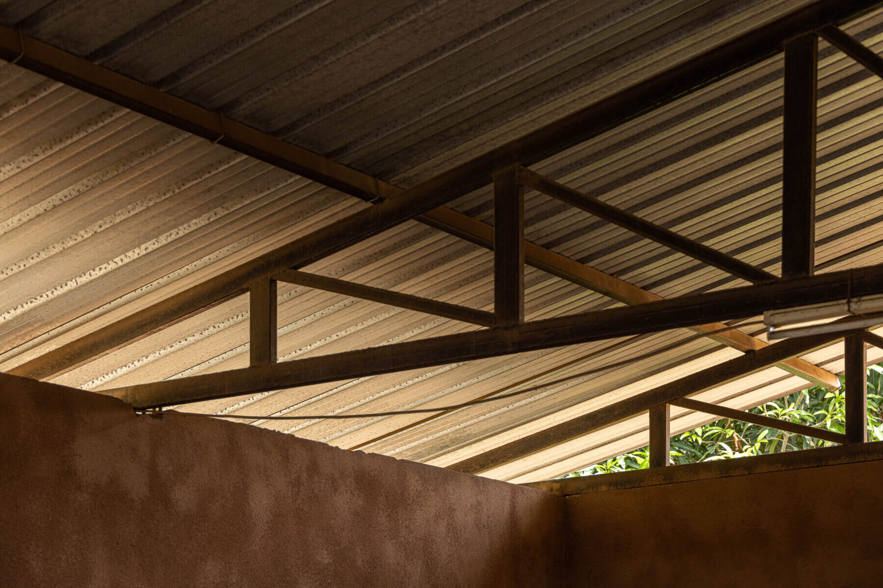 Detalhe do teto metálico aparente, com estrutura de suporte em ferro e revestimento em chapa ondulada. — Escola Kapalanga arquitetura Paulo Moreira Architectures e PARQ Arquitectos em Luanda