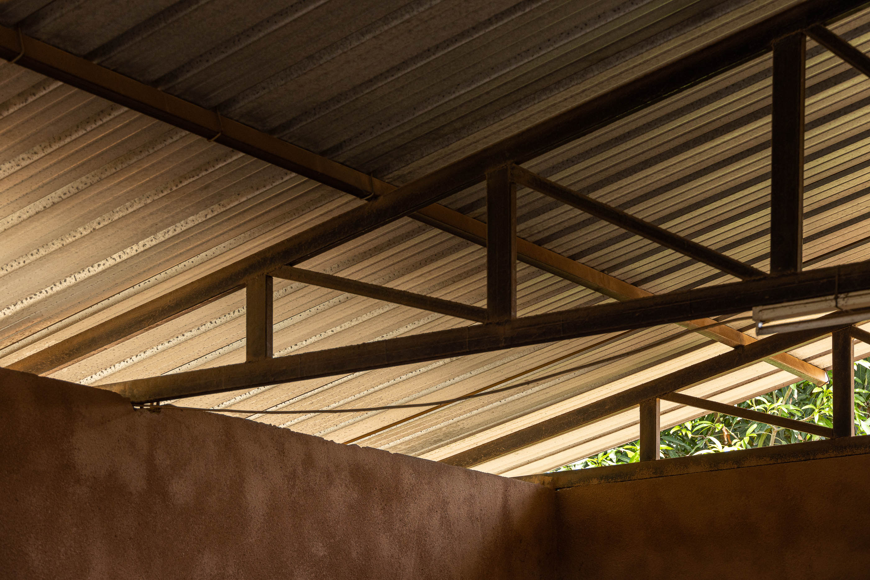 Detalhe do teto metálico aparente, com estrutura de suporte em ferro e revestimento em chapa ondulada. — Escola Kapalanga arquitetura Paulo Moreira Architectures e PARQ Arquitectos em Luanda