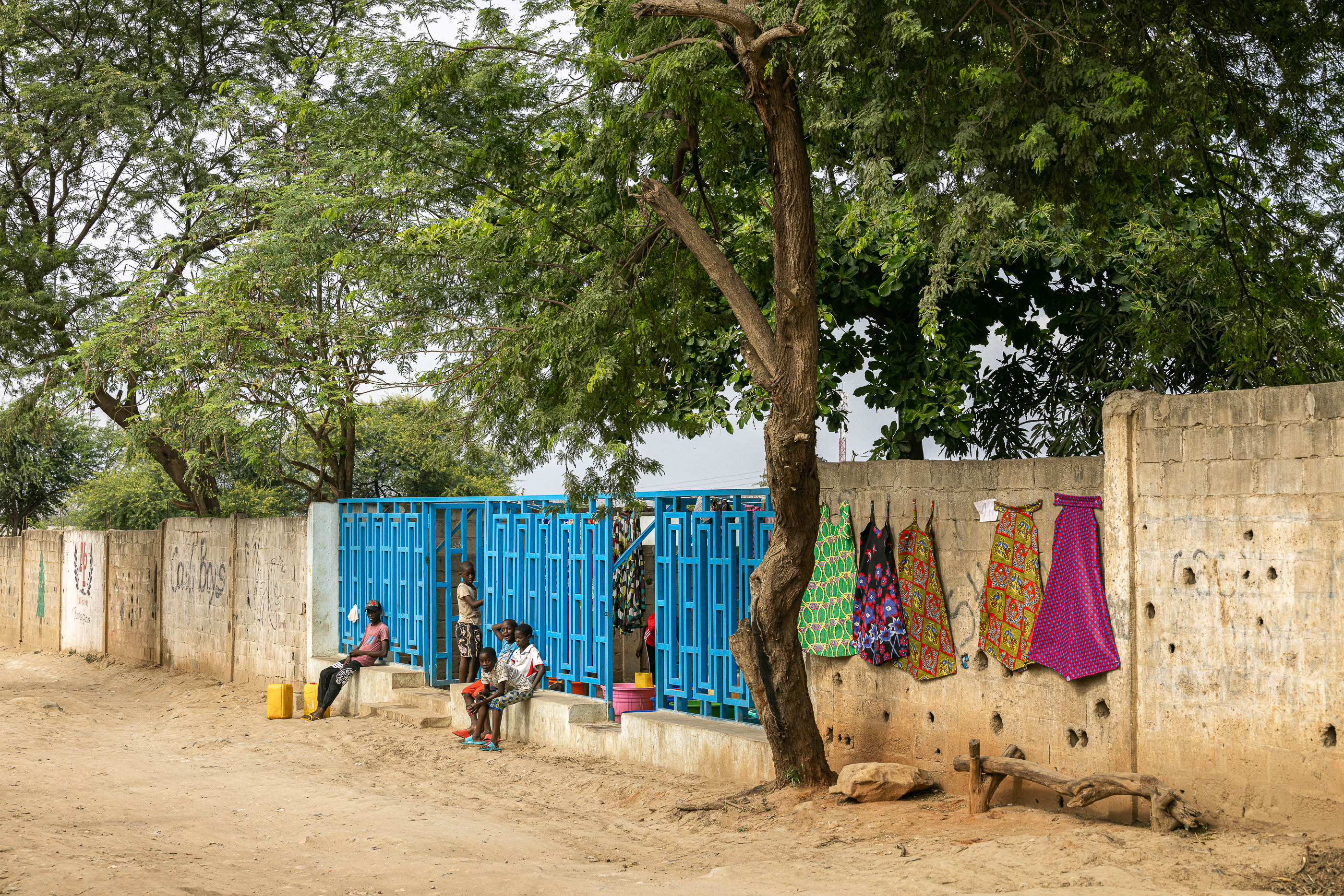 Exterior: Chafariz azul com pessoas a recolher água, roupa pendurada e muro de blocos de cimento. — Chafarizes em Luanda arquitetura Paulo Moreira Architectures em Luanda