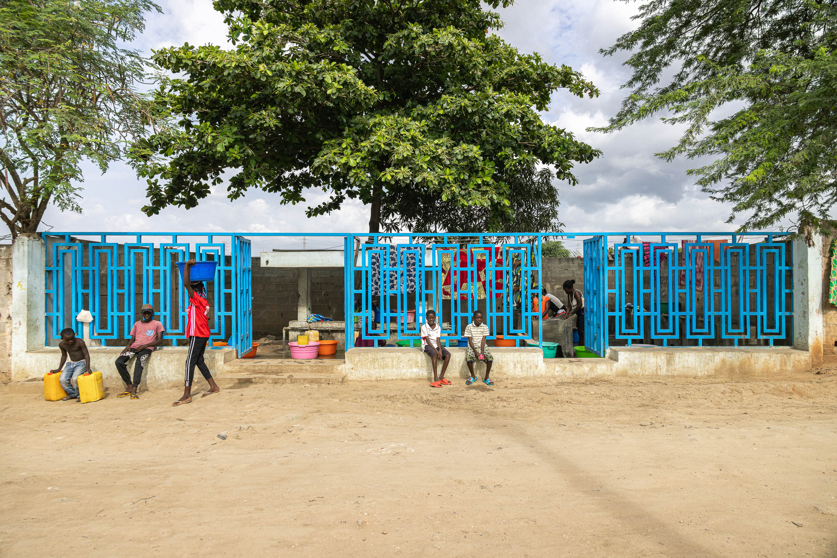 Exterior: Pessoas a recolher água num chafariz azul com cobertura, sentadas em bancos de cimento. — Chafarizes em Luanda arquitetura Paulo Moreira Architectures em Luanda