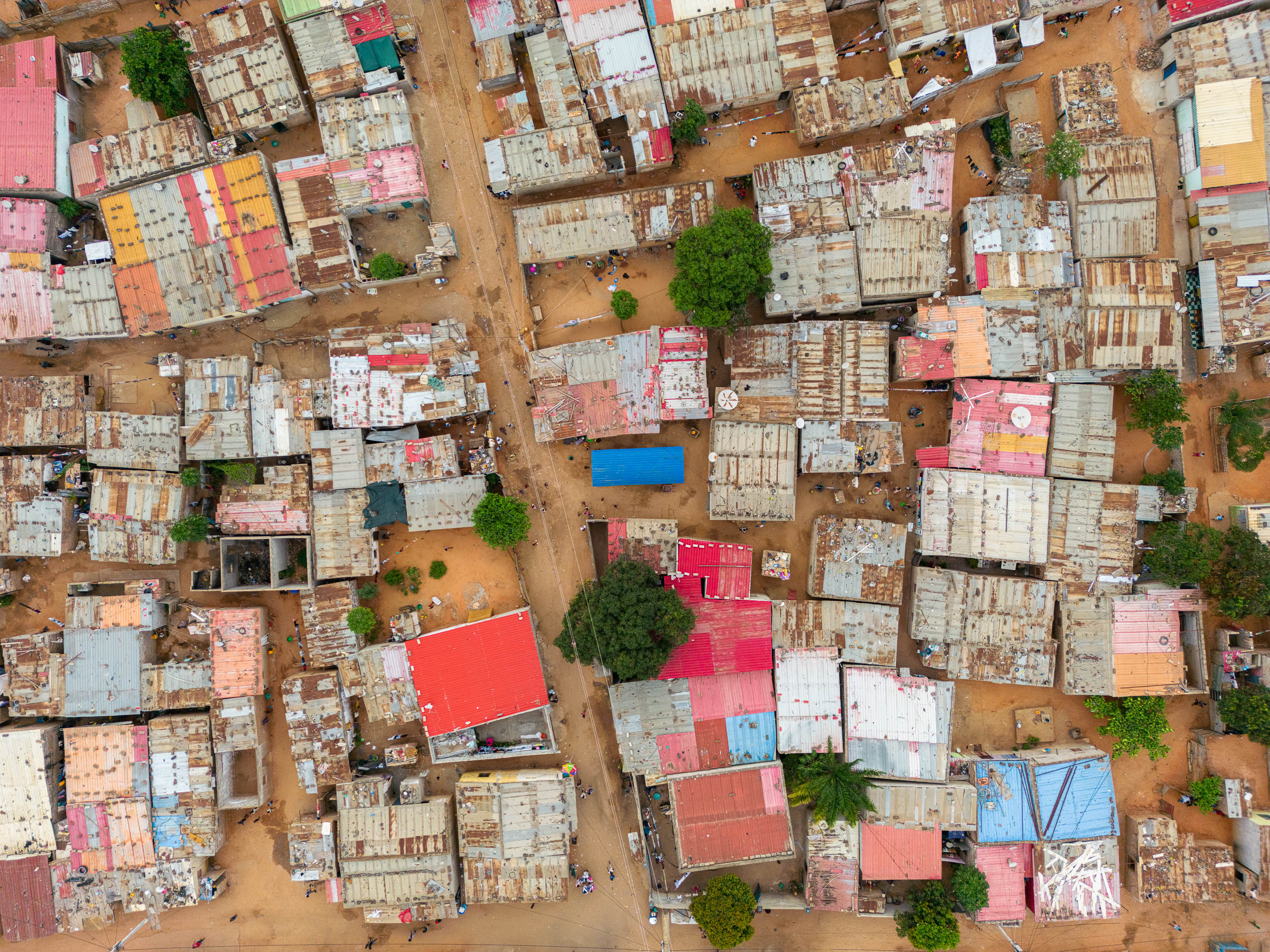 Telhados: Vista aérea de casas com telhados de zinco coloridos, ruas de terra batida e vegetação. — Chafarizes em Luanda arquitetura Paulo Moreira Architectures em Luanda