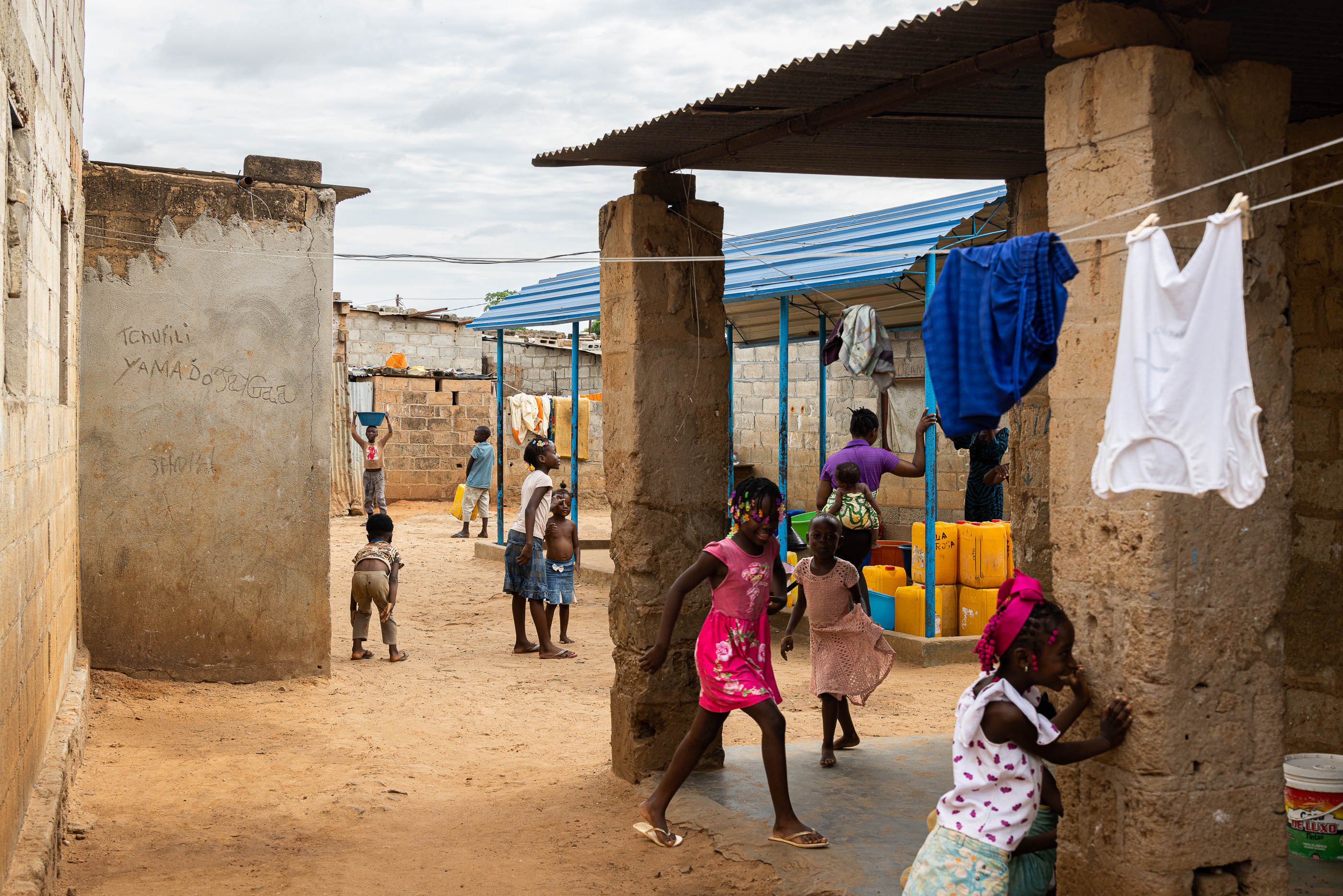 Exterior: Crianças a brincar perto de um chafariz, com roupa a secar e paredes de blocos de cimento. — Chafarizes em Luanda arquitetura Paulo Moreira Architectures em Luanda
