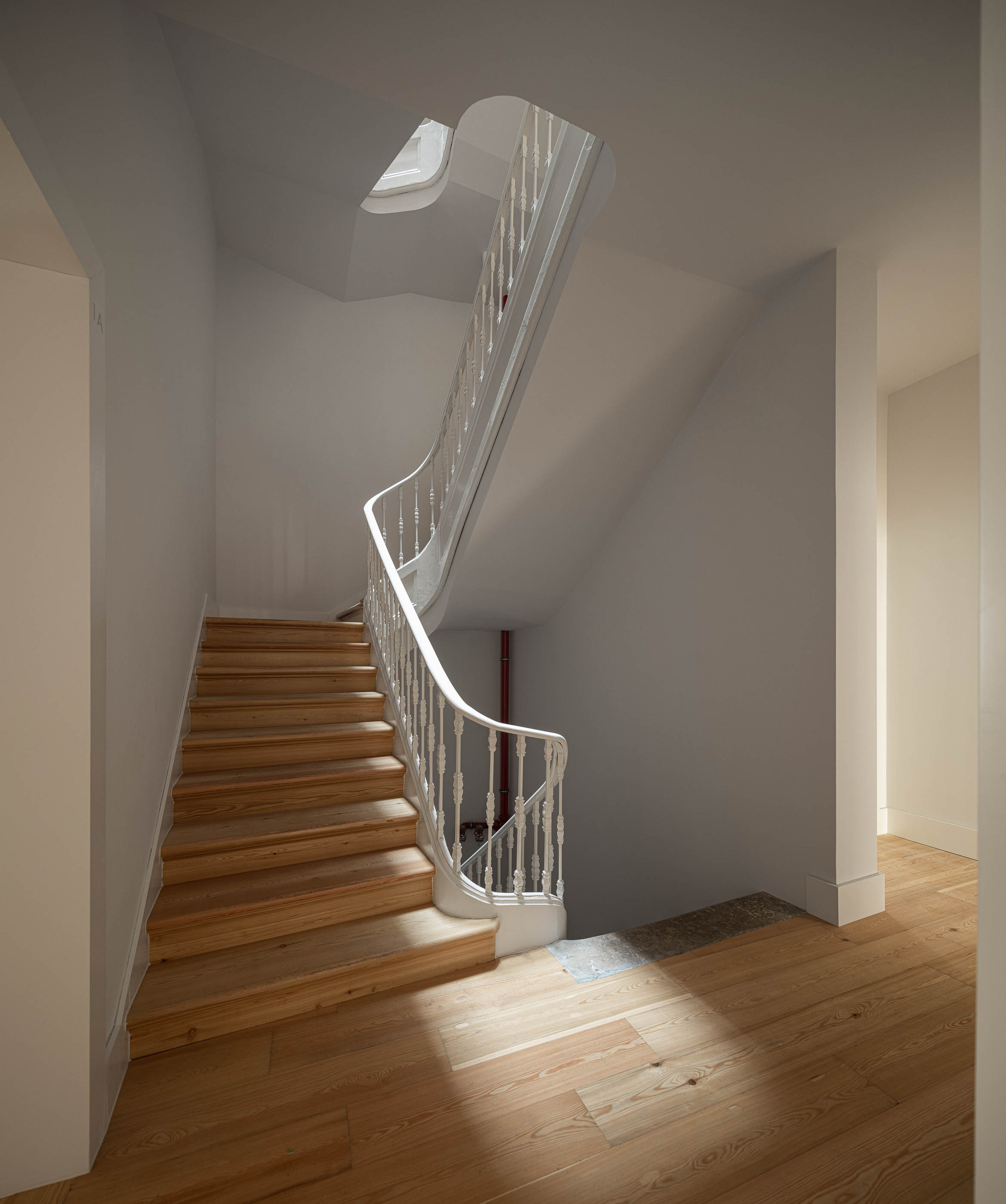Escadaria: Escadaria com degraus em madeira clara, corrimão branco e paredes brancas, iluminada por luz natural. — Victor Cordon arquitetura Fragmentos em Lisboa