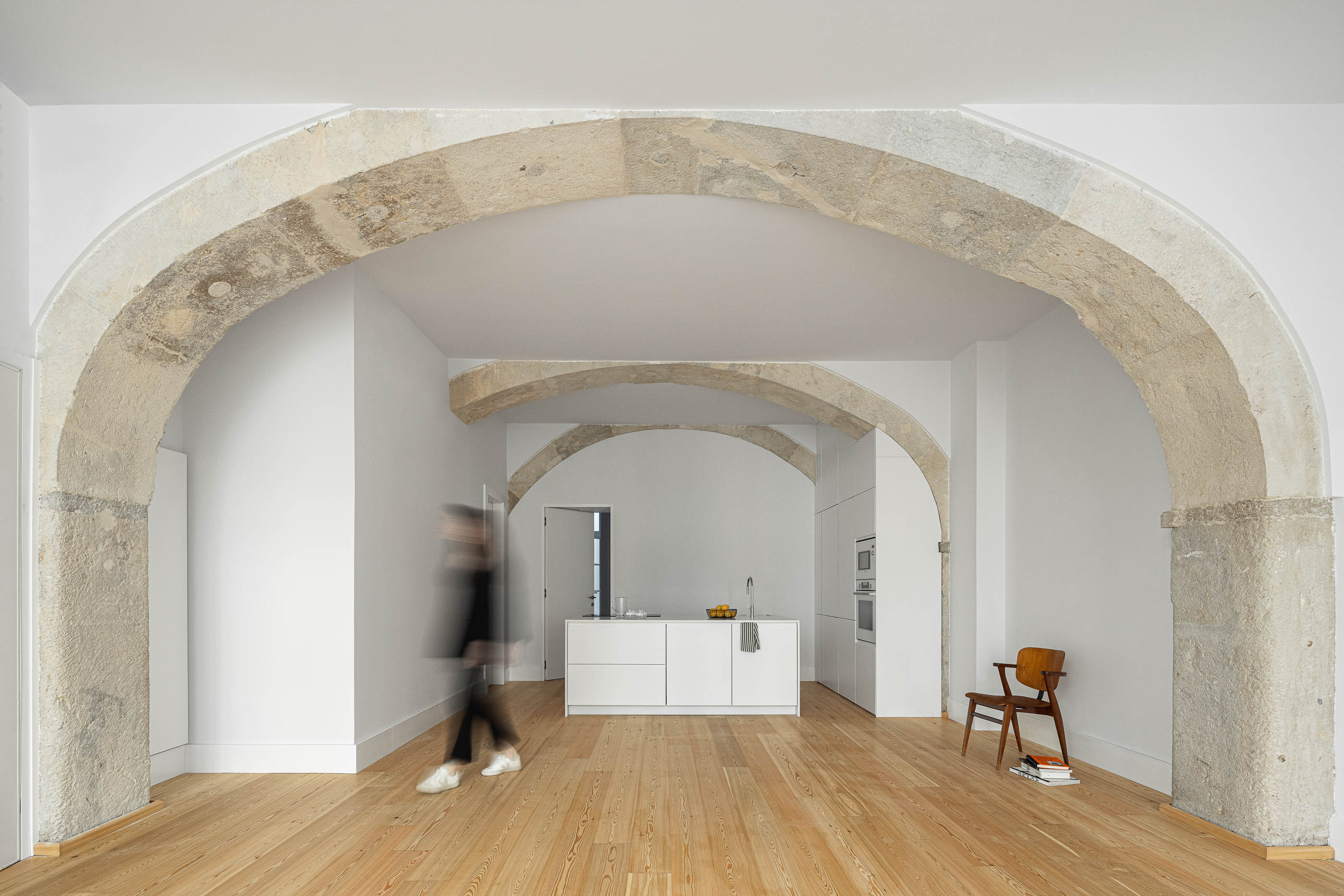 Sala de estar: Espaço amplo com arcos de pedra originais, pavimento em madeira clara e paredes brancas. — Victor Cordon arquitetura Fragmentos em Lisboa