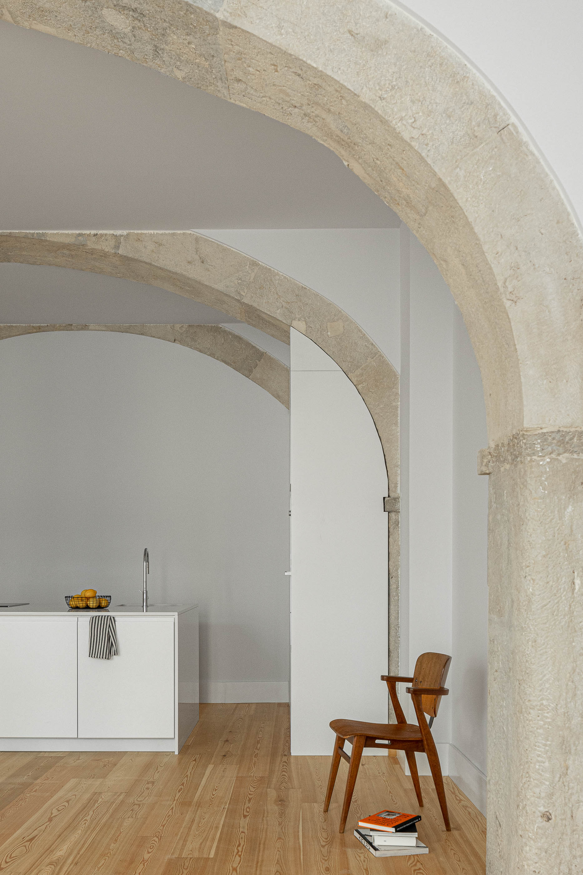 Sala de estar: Detalhe dos arcos de pedra, pavimento em madeira clara e cadeira de madeira vintage. — Victor Cordon arquitetura Fragmentos em Lisboa