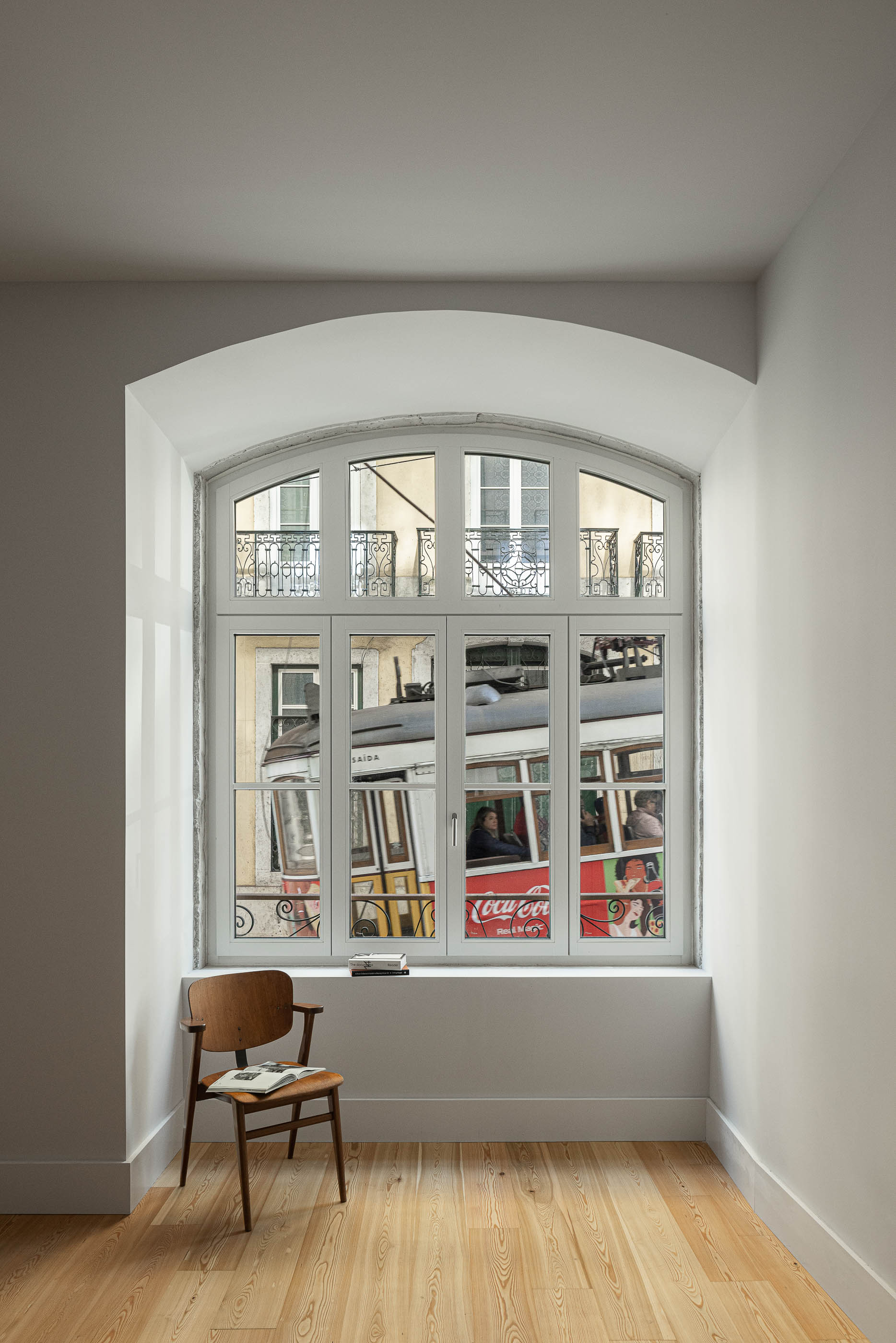 Sala de estar: Janela de sacada com vista para a rua, pavimento em madeira clara e cadeira vintage. — Victor Cordon arquitetura Fragmentos em Lisboa