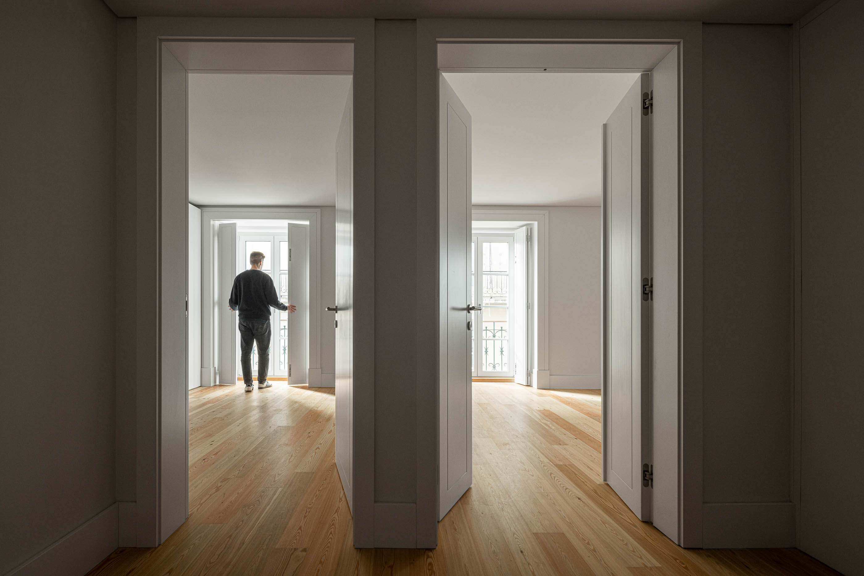 Corredor: Corredor com portas brancas, pavimento em madeira clara e vista para quartos adjacentes. — Victor Cordon arquitetura Fragmentos em Lisboa