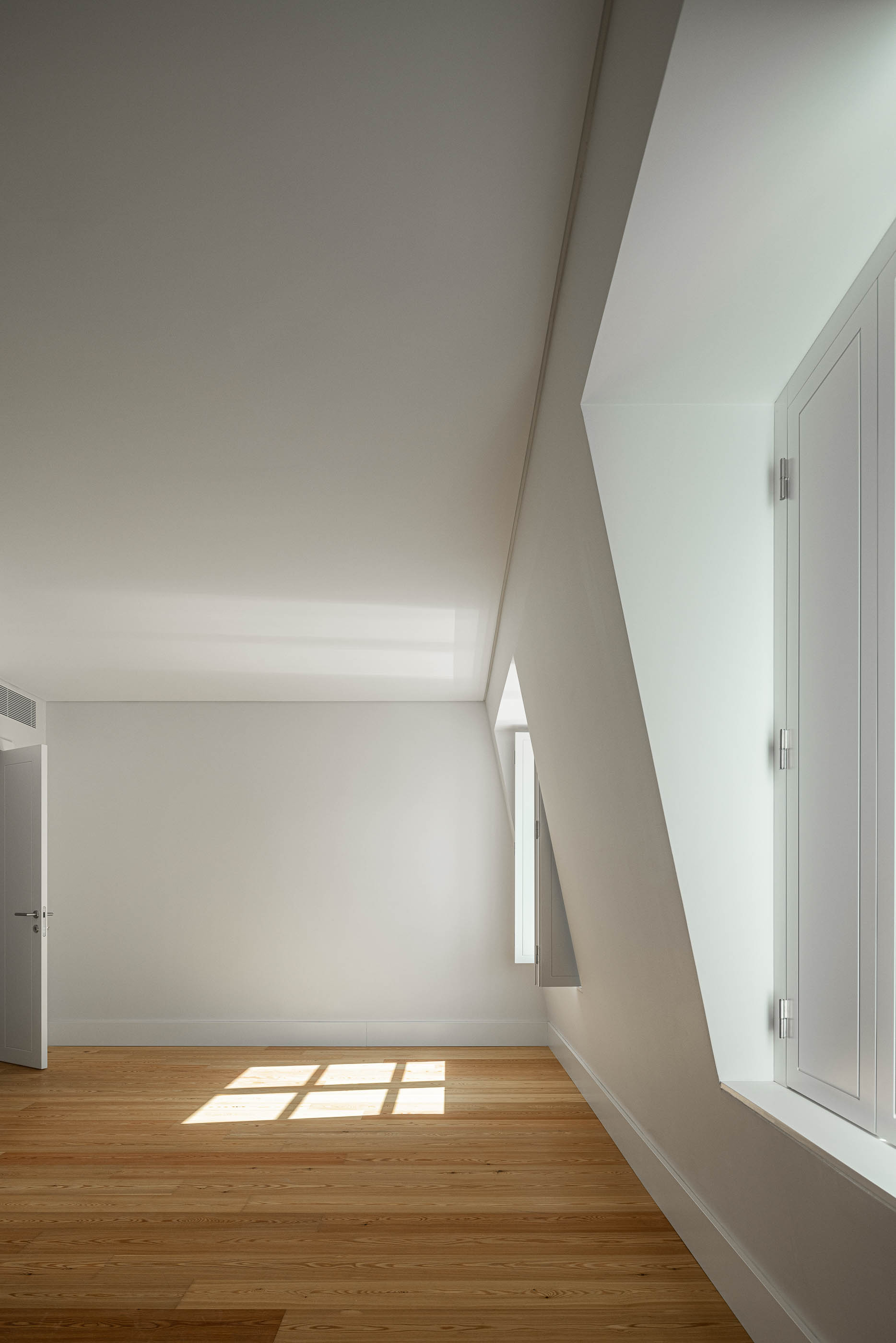 Quarto: Quarto com pavimento em madeira clara, paredes brancas e janelas com design moderno. — Victor Cordon arquitetura Fragmentos em Lisboa