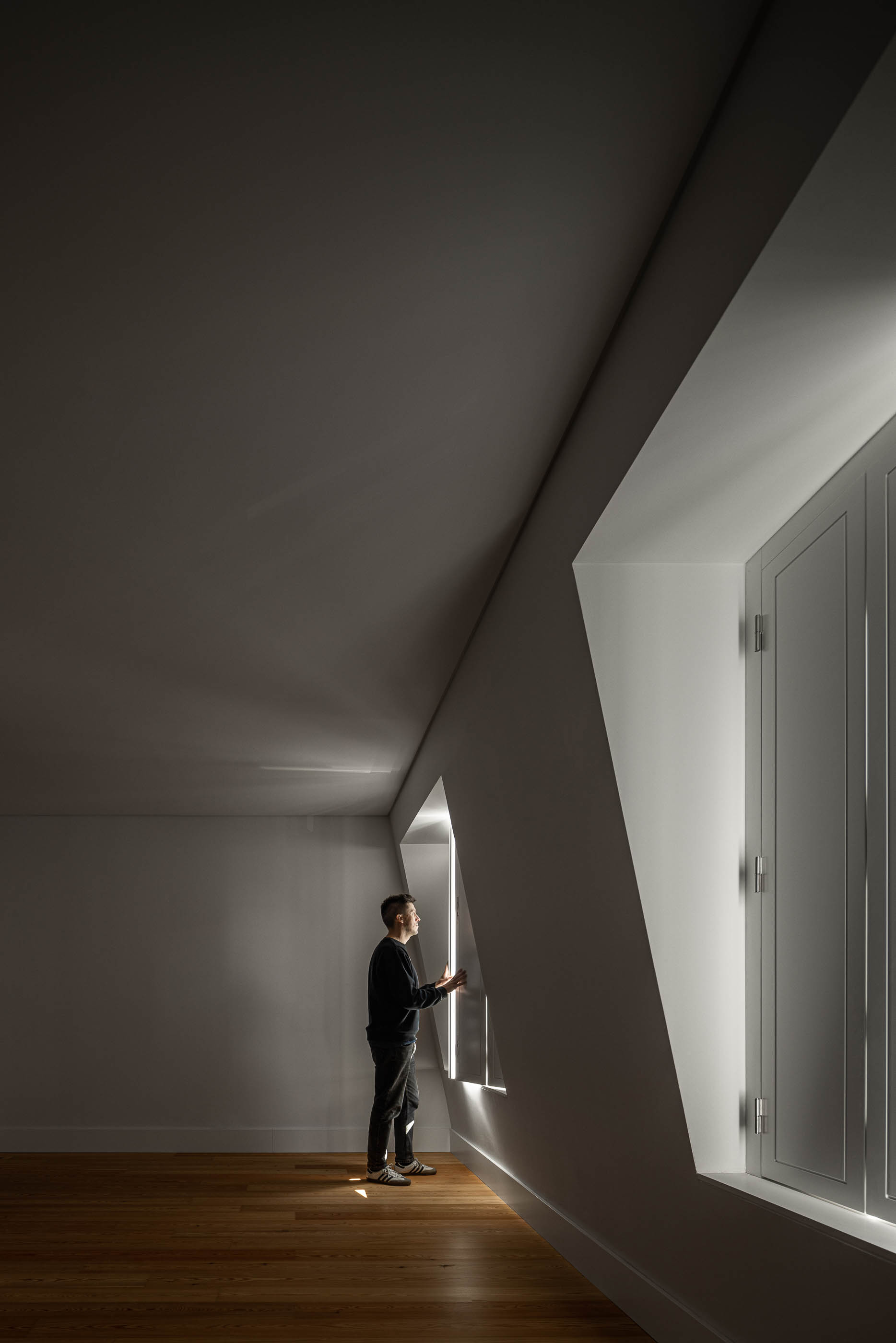 Quarto: Quarto com pavimento em madeira clara, paredes brancas e janelas com design angular. — Victor Cordon arquitetura Fragmentos em Lisboa