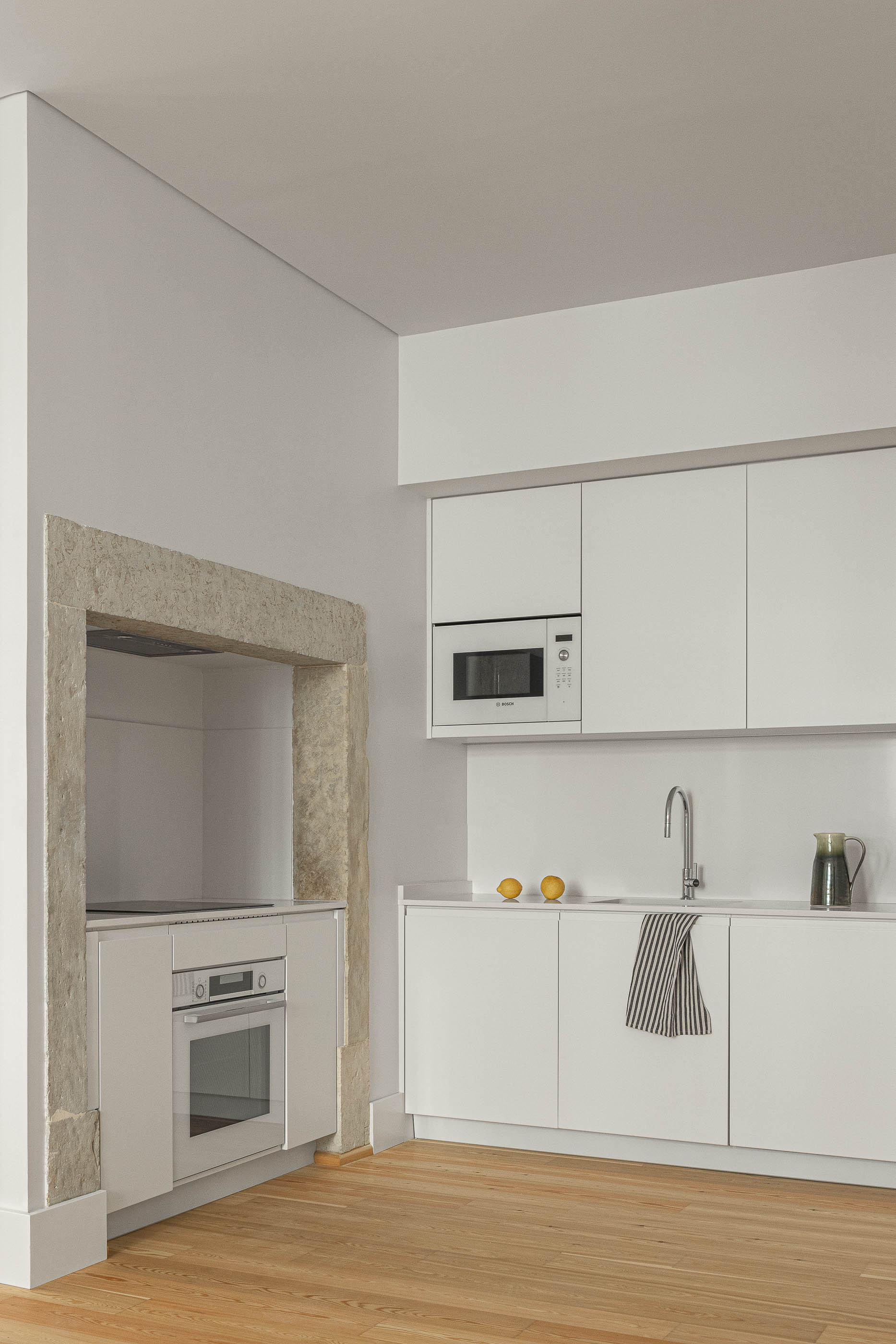 Cozinha: Cozinha moderna com armários brancos minimalistas e arcos de pedra originais. — Victor Cordon arquitetura Fragmentos em Lisboa