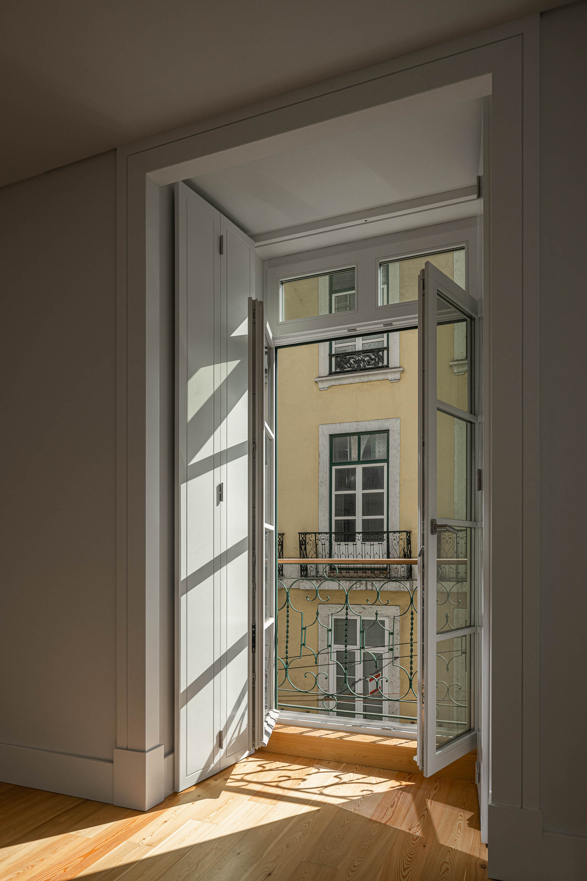 Varanda: Vista da varanda com porta envidraçada, pavimento em madeira clara e gradeamento em ferro. — Victor Cordon arquitetura Fragmentos em Lisboa