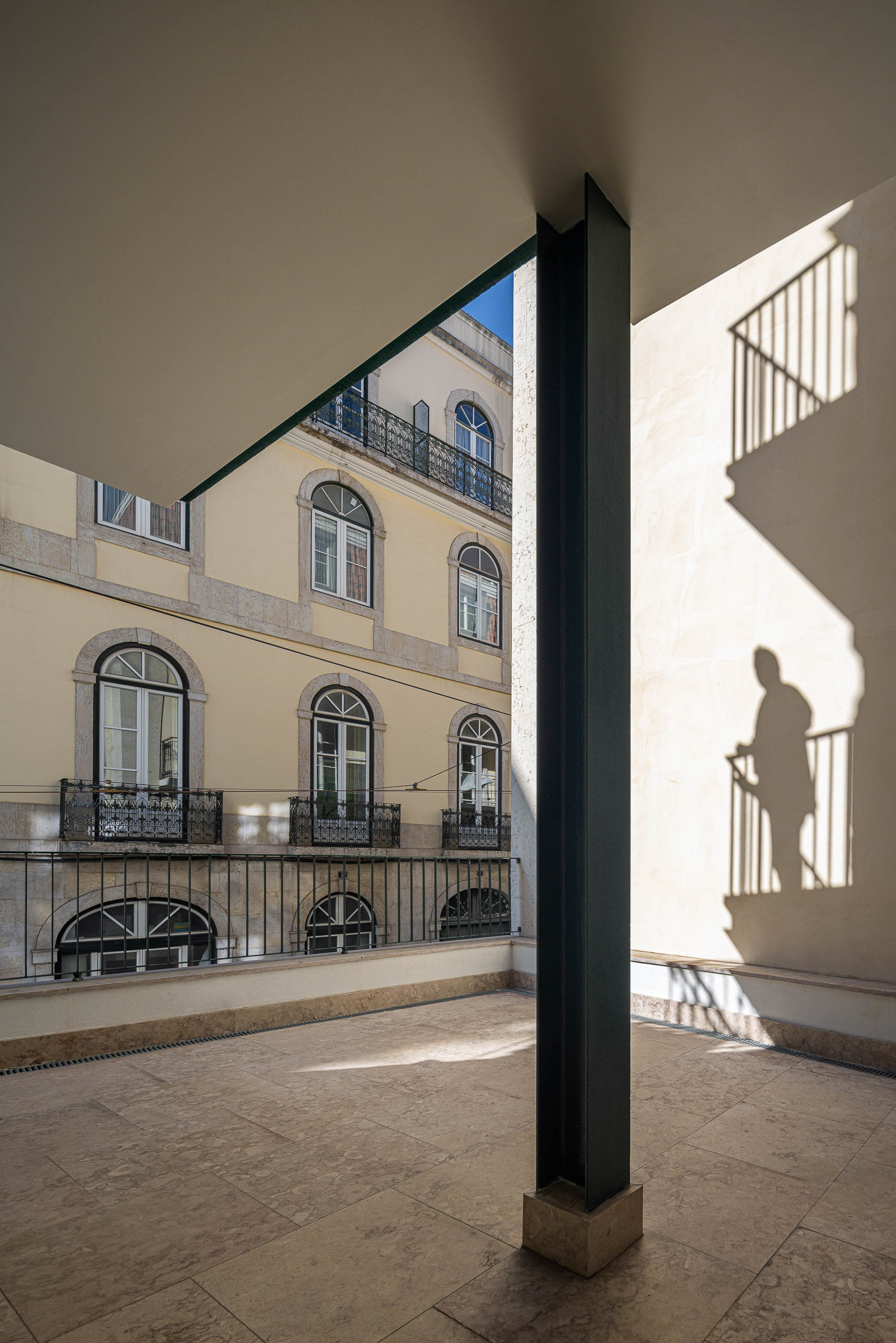 Varanda: Varanda com pavimento em pedra clara, pilar metálico e vista para edifícios históricos. — Victor Cordon arquitetura Fragmentos em Lisboa