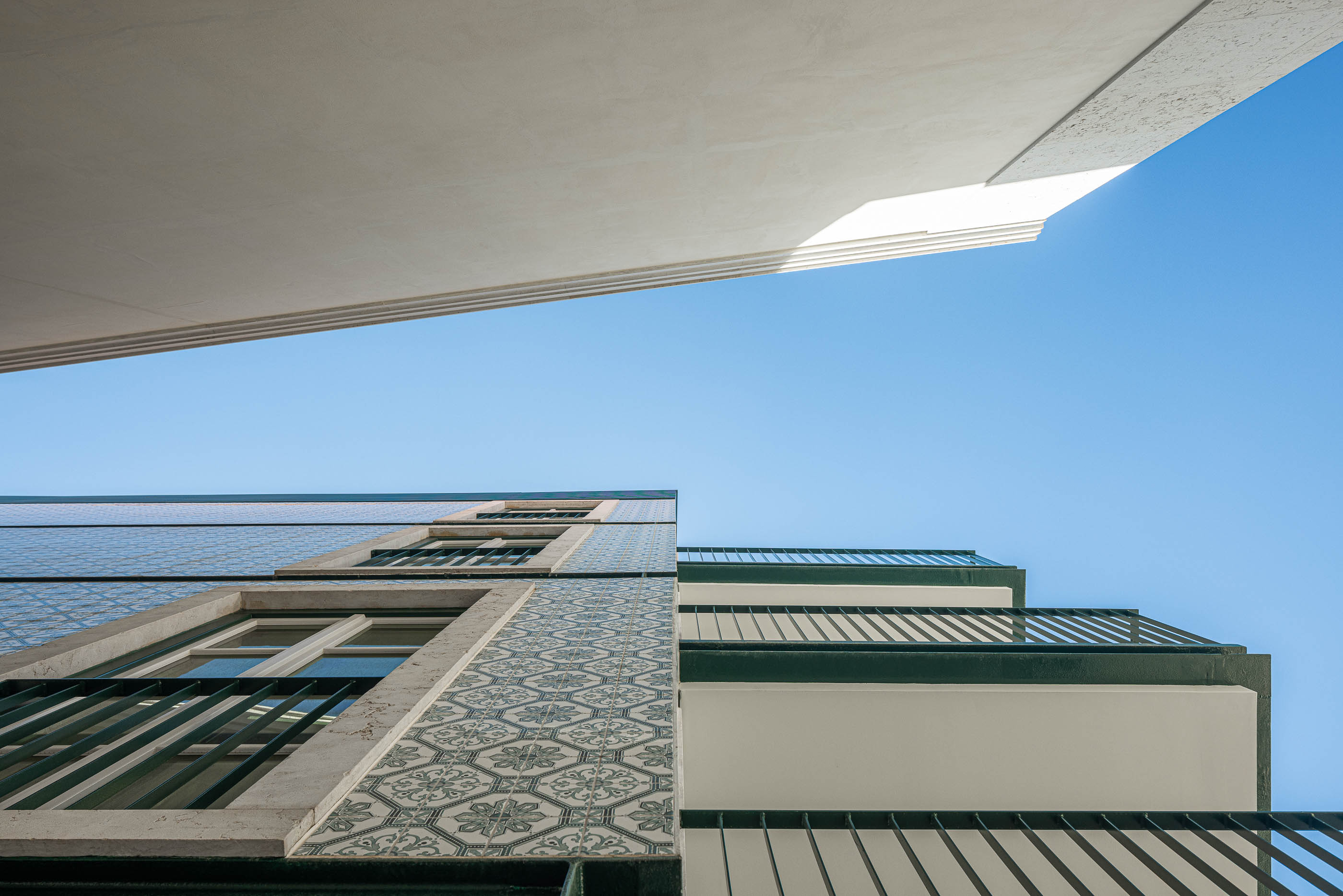 Fachada: Vista ascendente da fachada com azulejos decorativos, varandas em ferro forjado e céu azul. — Victor Cordon arquitetura Fragmentos em Lisboa