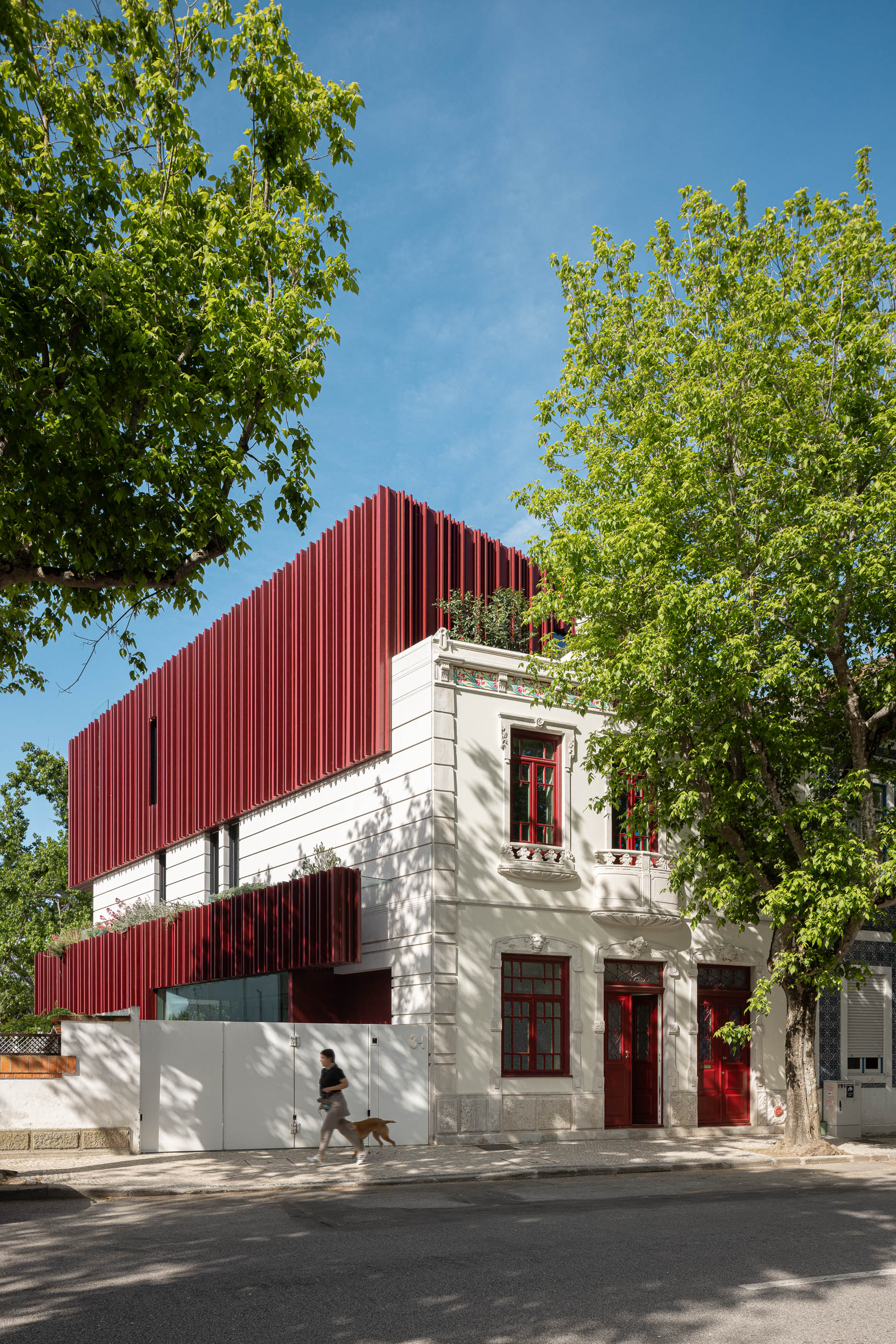 Fachada: Vista exterior da casa com revestimento vertical vermelho e detalhes clássicos, sob um céu azul. — Casa do Parque arquitetura Paulo Martins Arquitectura e Design em Aveiro