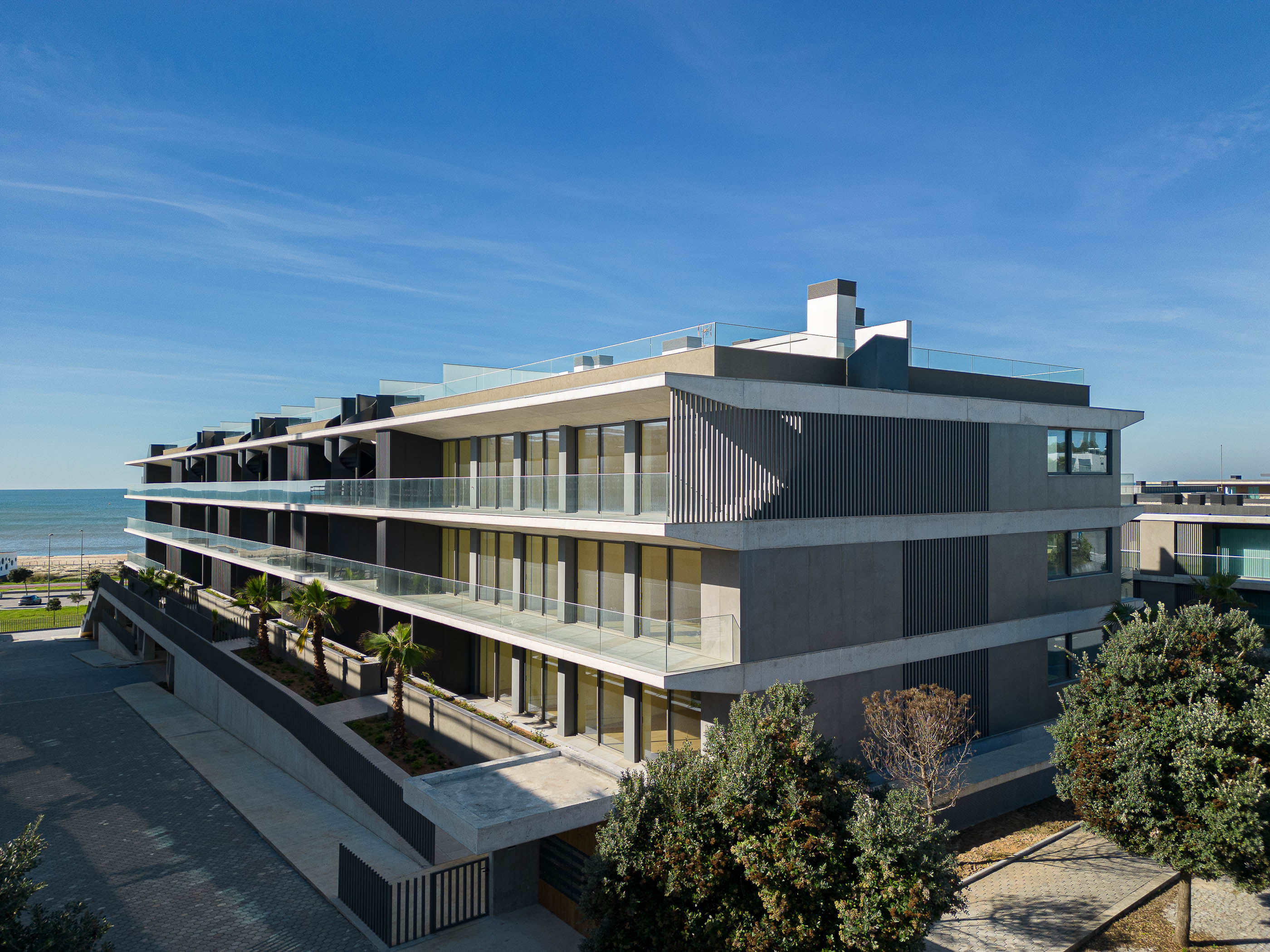Edifício: Fachada com varandas em betão e vidro, com brises verticais e vista para o mar. — Edifício Seashore arquitetura Atelier d´Arquitectura Lopes da Costa em Vila Nova de Gaia