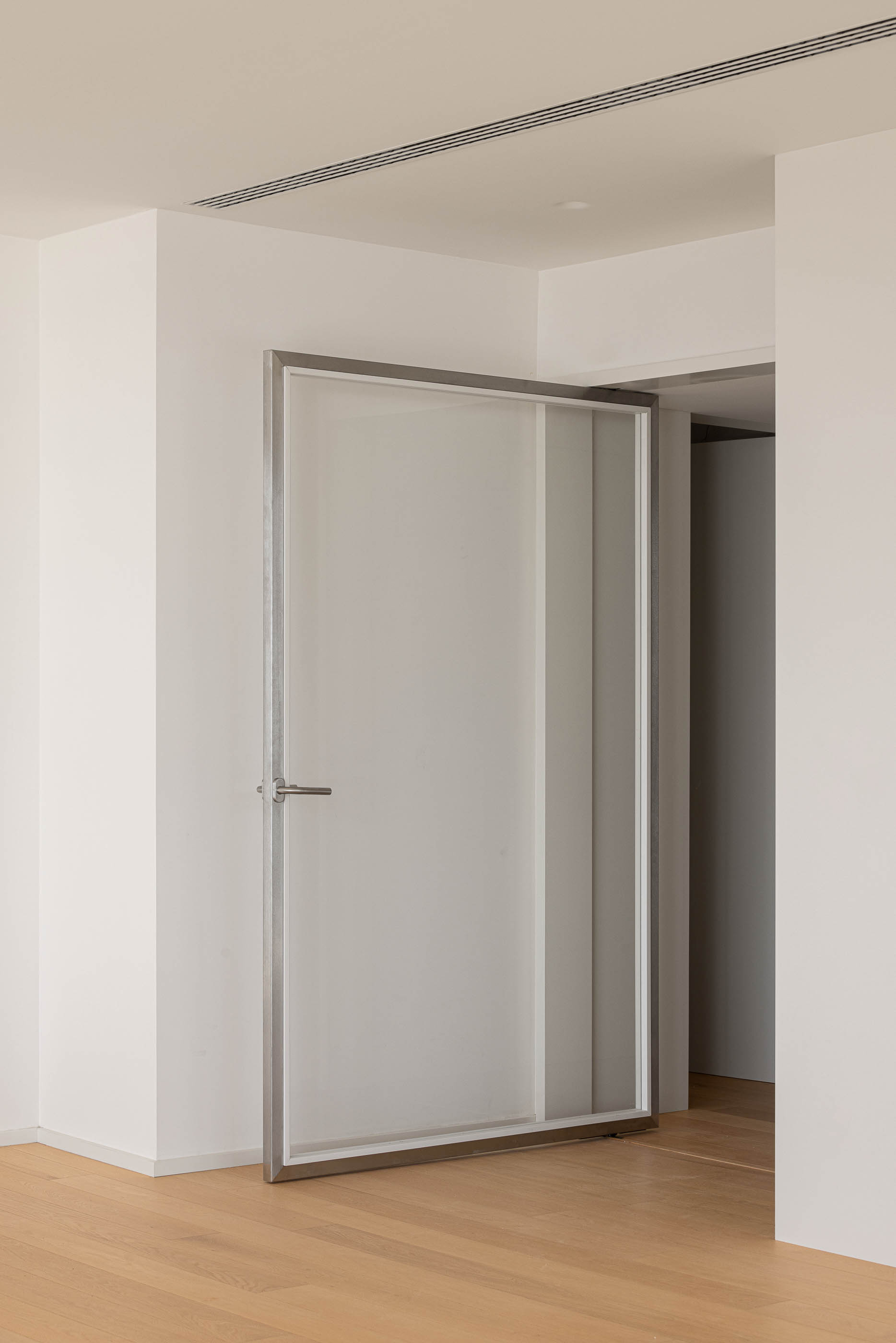 Sala de estar: Porta pivotante com estrutura metálica e pavimento em madeira. — Edifício Seashore arquitetura Atelier d´Arquitectura Lopes da Costa em Vila Nova de Gaia