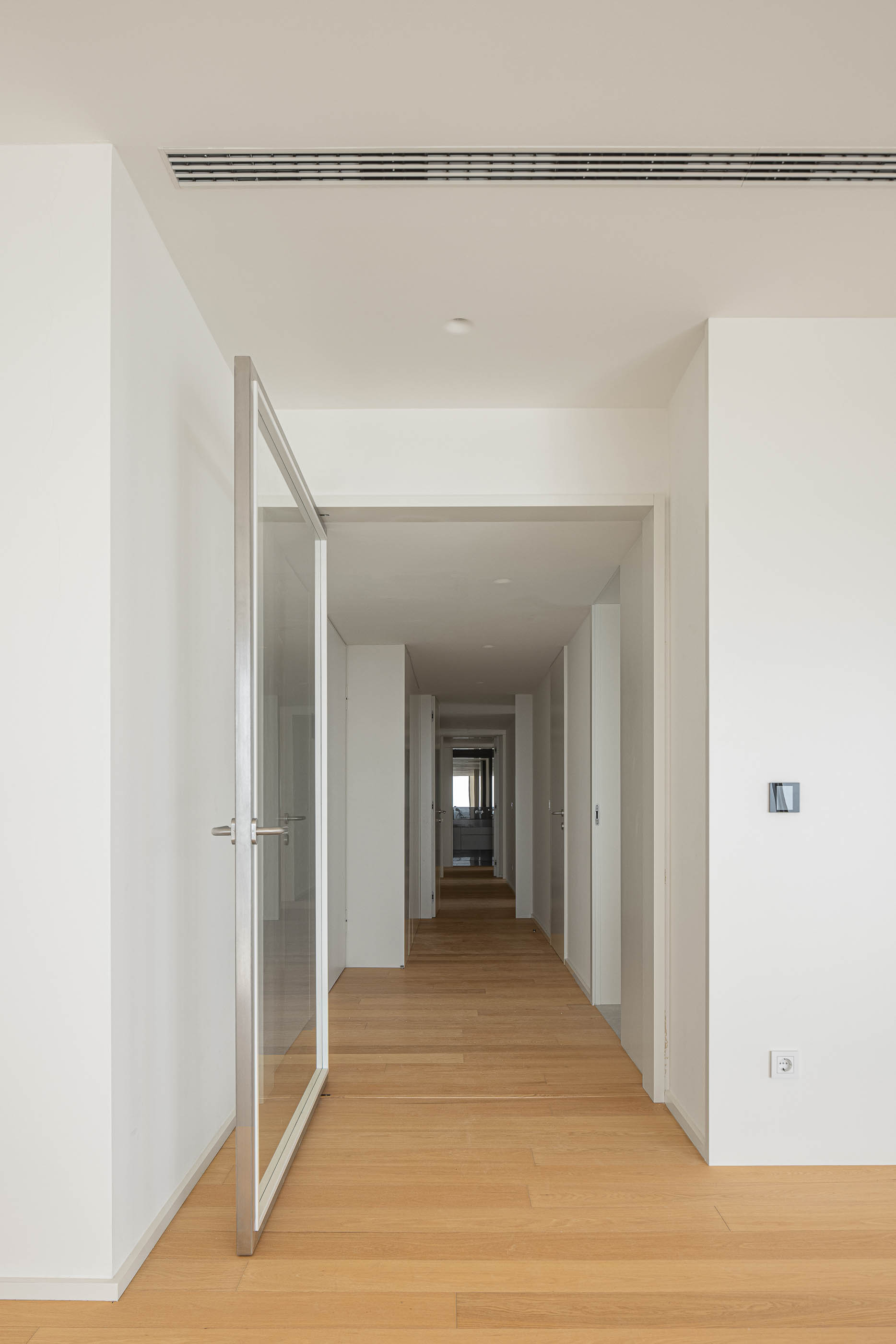 Corredor: Longo corredor com pavimento em madeira, portas brancas e pivotantes. — Edifício Seashore arquitetura Atelier d´Arquitectura Lopes da Costa em Vila Nova de Gaia
