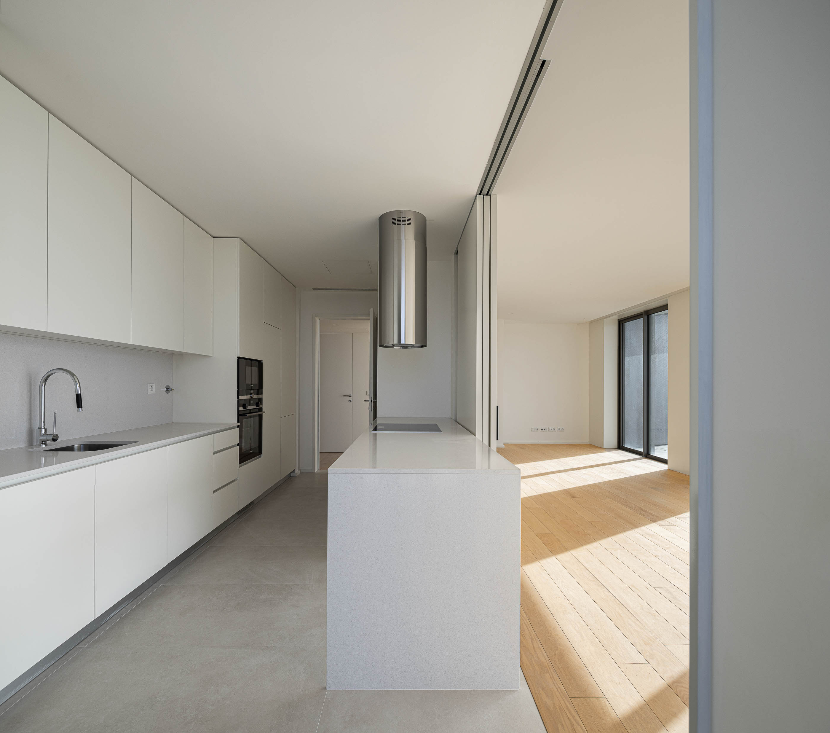 Cozinha: Ilha central, armários lacados brancos e pavimento cerâmico. — Edifício Seashore arquitetura Atelier d´Arquitectura Lopes da Costa em Vila Nova de Gaia