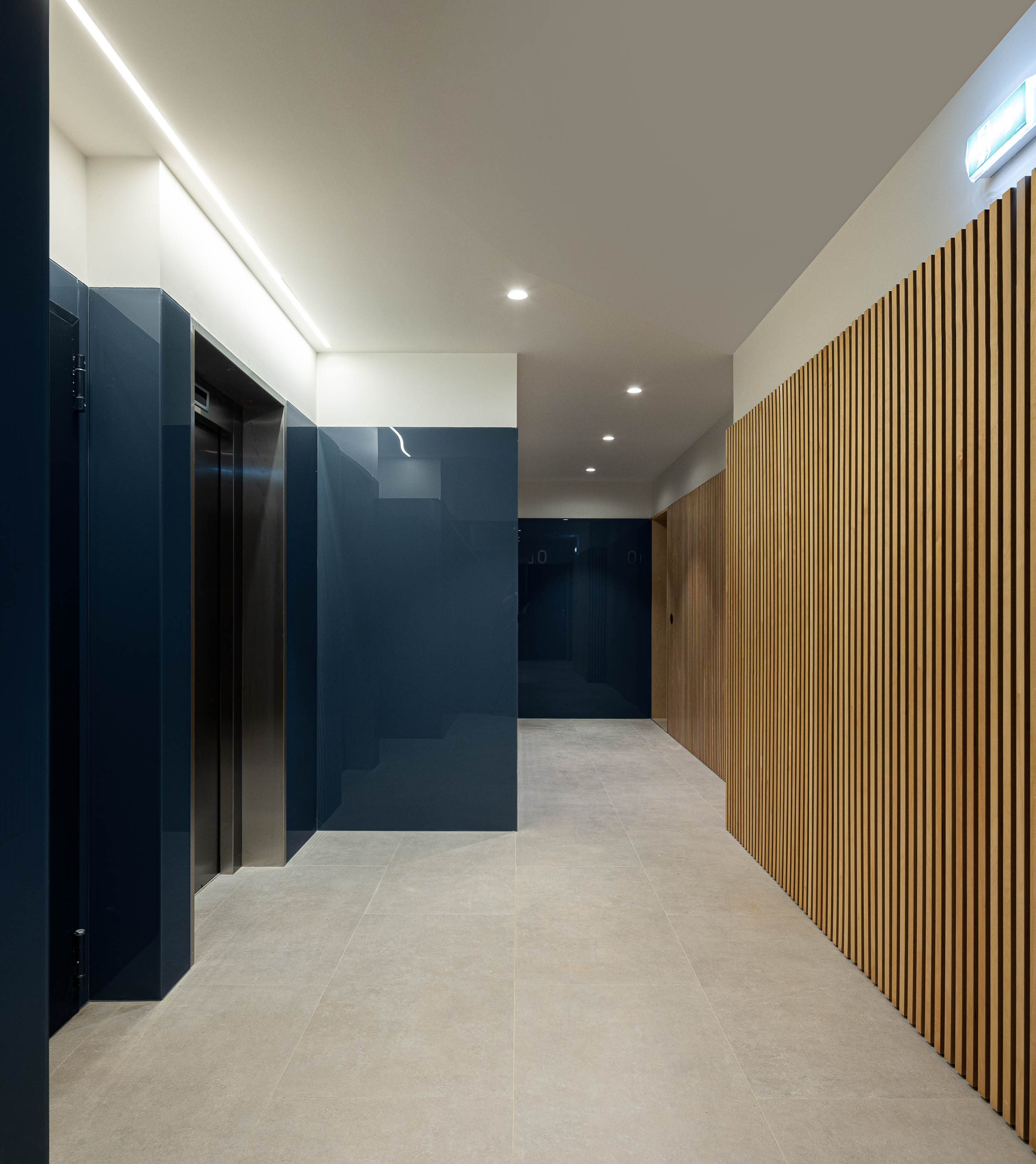 Hall de entrada: Corredor com elevador, paredes em azul e madeira, pavimento cerâmico. — Edifício Seashore arquitetura Atelier d´Arquitectura Lopes da Costa em Vila Nova de Gaia