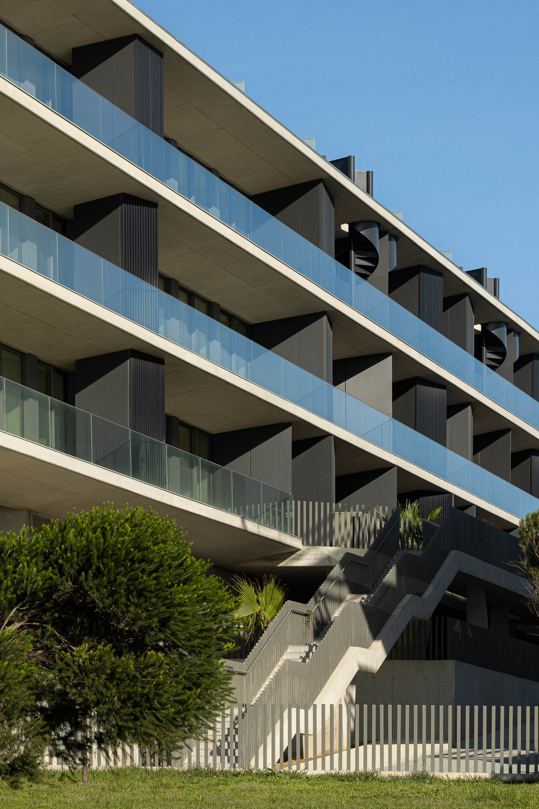 Edifício: Fachada com varandas em betão e vidro, escada exterior e vegetação. — Edifício Seashore arquitetura Atelier d´Arquitectura Lopes da Costa em Vila Nova de Gaia