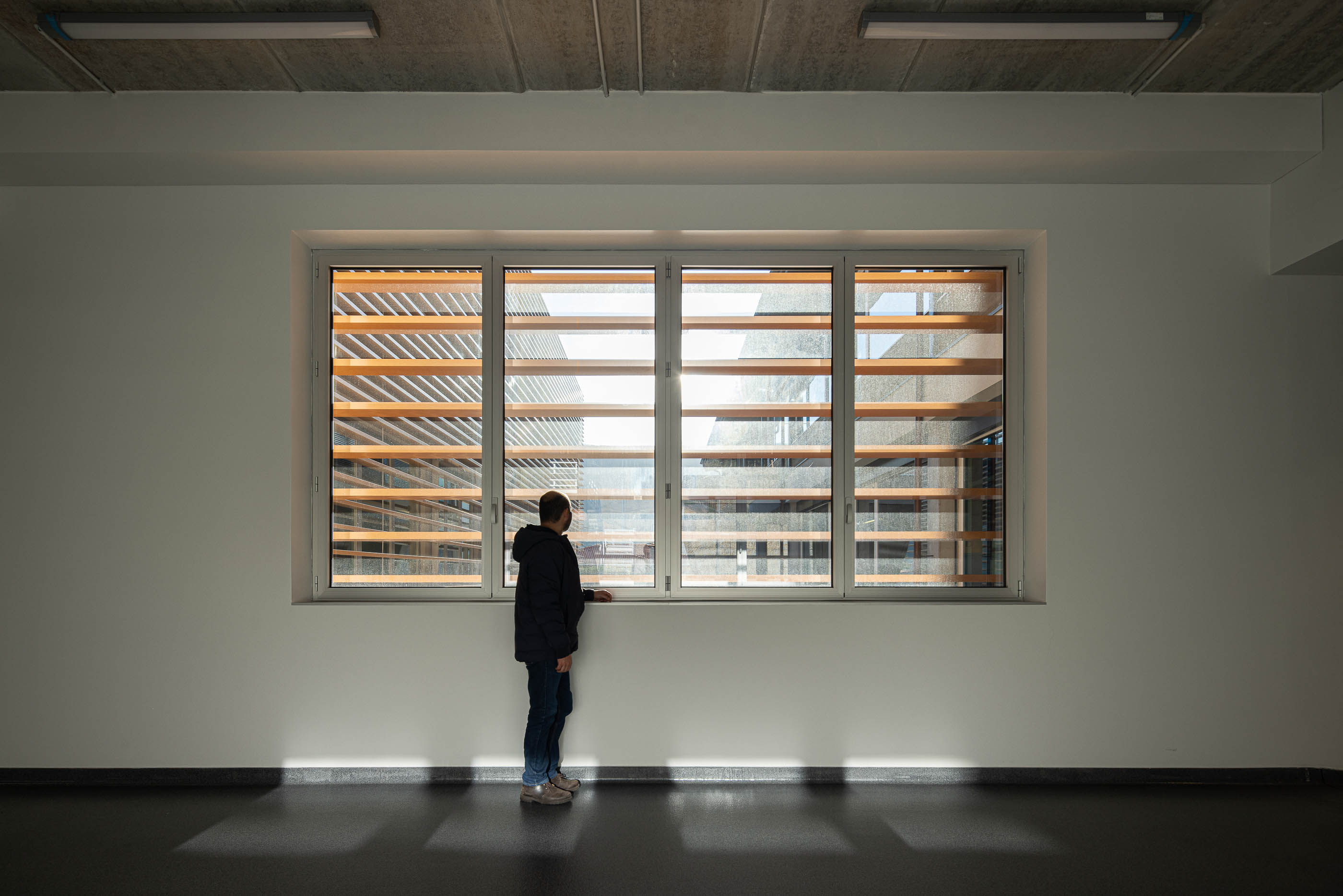 Escritório: Interior com pavimento escuro, paredes brancas e janela com vista para a fachada do edifício. — Unidade Industrial OROPOL arquitetura Em Paralelo em Castelo de Paiva