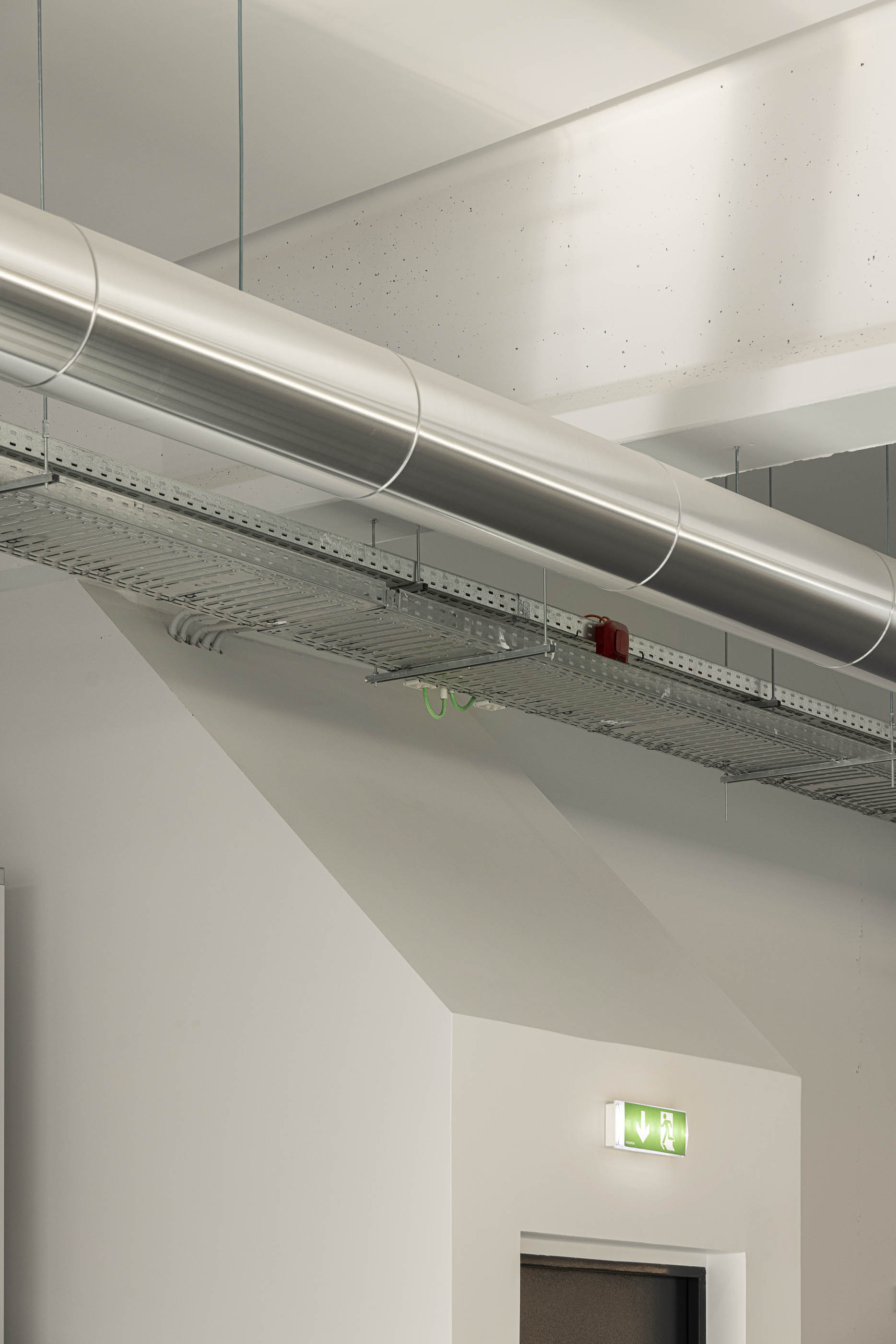 Teto: Detalhe do teto com tubagens industriais aparentes e iluminação. — Unidade Industrial OROPOL arquitetura Em Paralelo em Castelo de Paiva