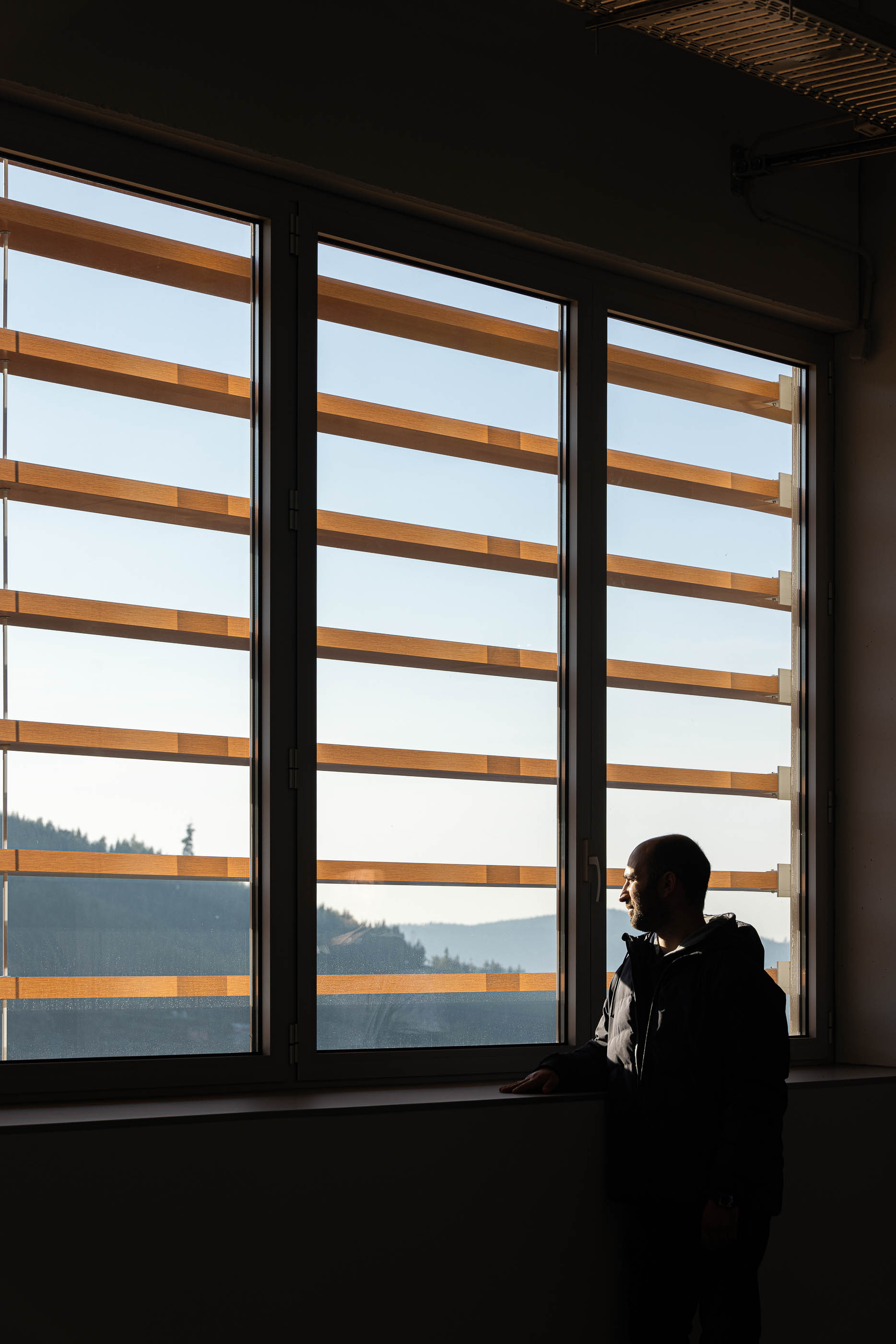 Escritório: Homem junto à janela com vista para a paisagem e fachada do edifício. — Unidade Industrial OROPOL arquitetura Em Paralelo em Castelo de Paiva