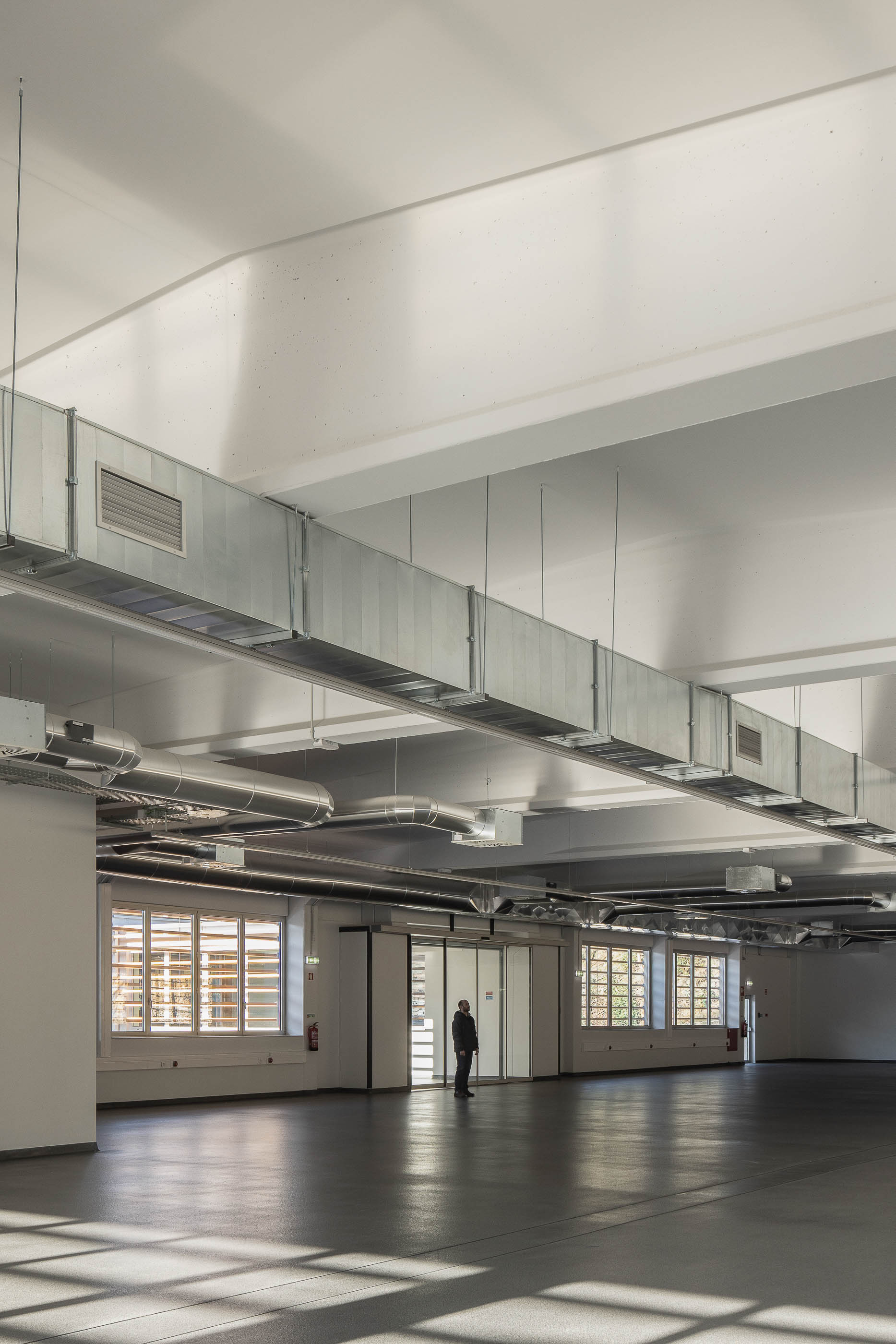 Armazém: Espaço industrial amplo com pavimento escuro, teto branco com tubagens e janelas com proteções solares. — Unidade Industrial OROPOL arquitetura Em Paralelo em Castelo de Paiva