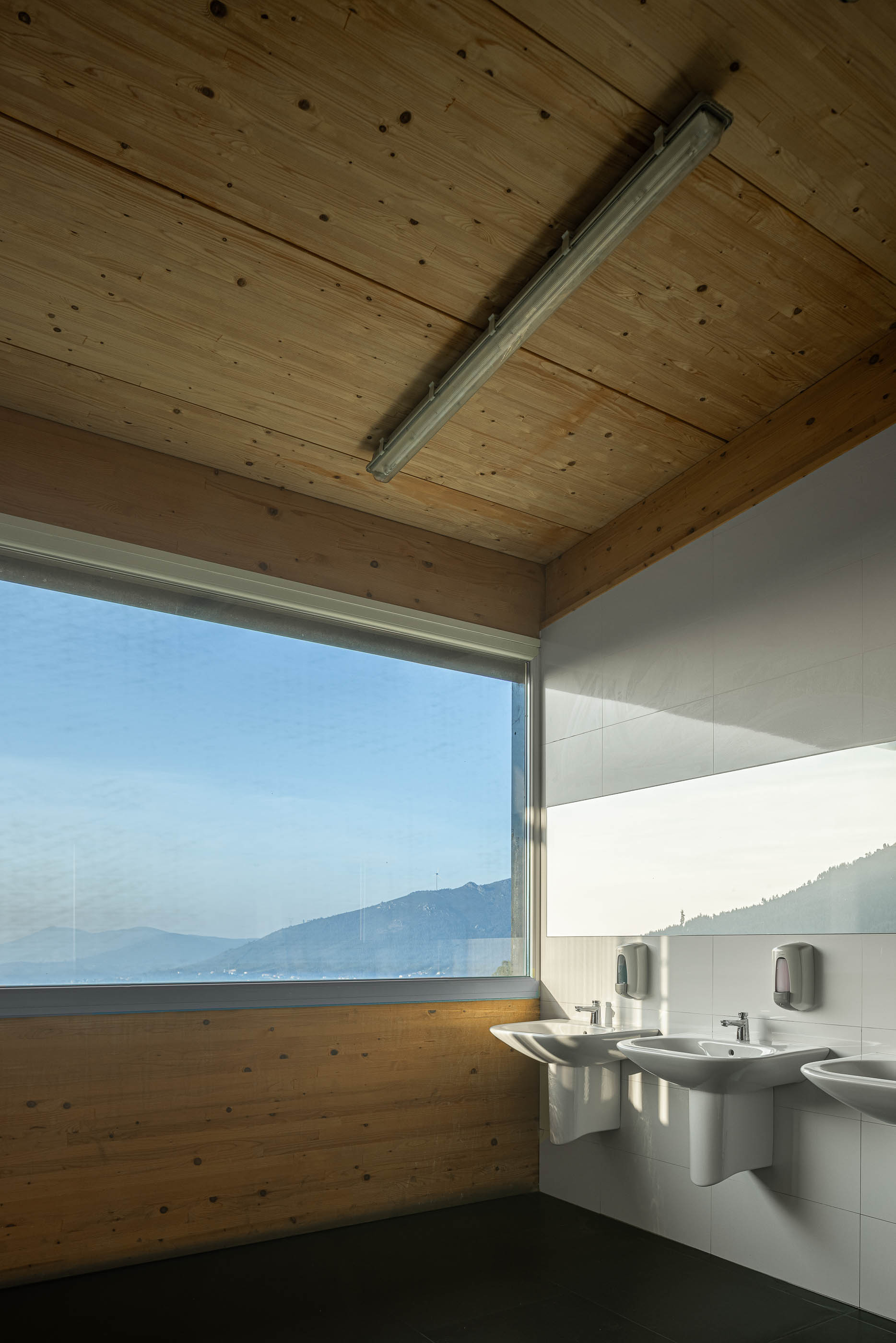 Casa de banho: Lavatórios em cerâmica branca com espelho e revestimento em madeira na parede. — Unidade Industrial OROPOL arquitetura Em Paralelo em Castelo de Paiva