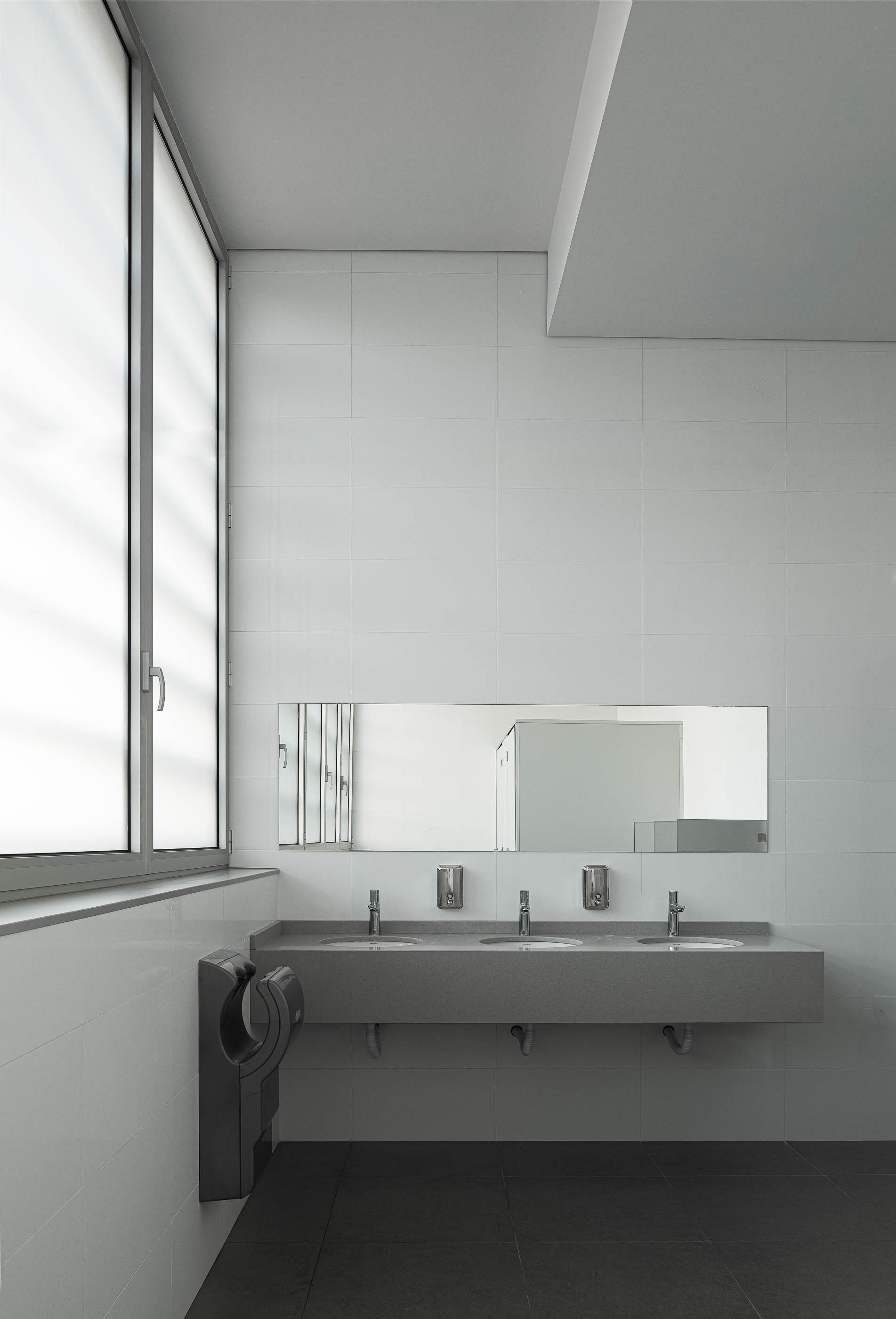 Casa de banho: Lavatórios em pedra cinzenta com espelho e revestimento cerâmico branco nas paredes. — Unidade Industrial OROPOL arquitetura Em Paralelo em Castelo de Paiva