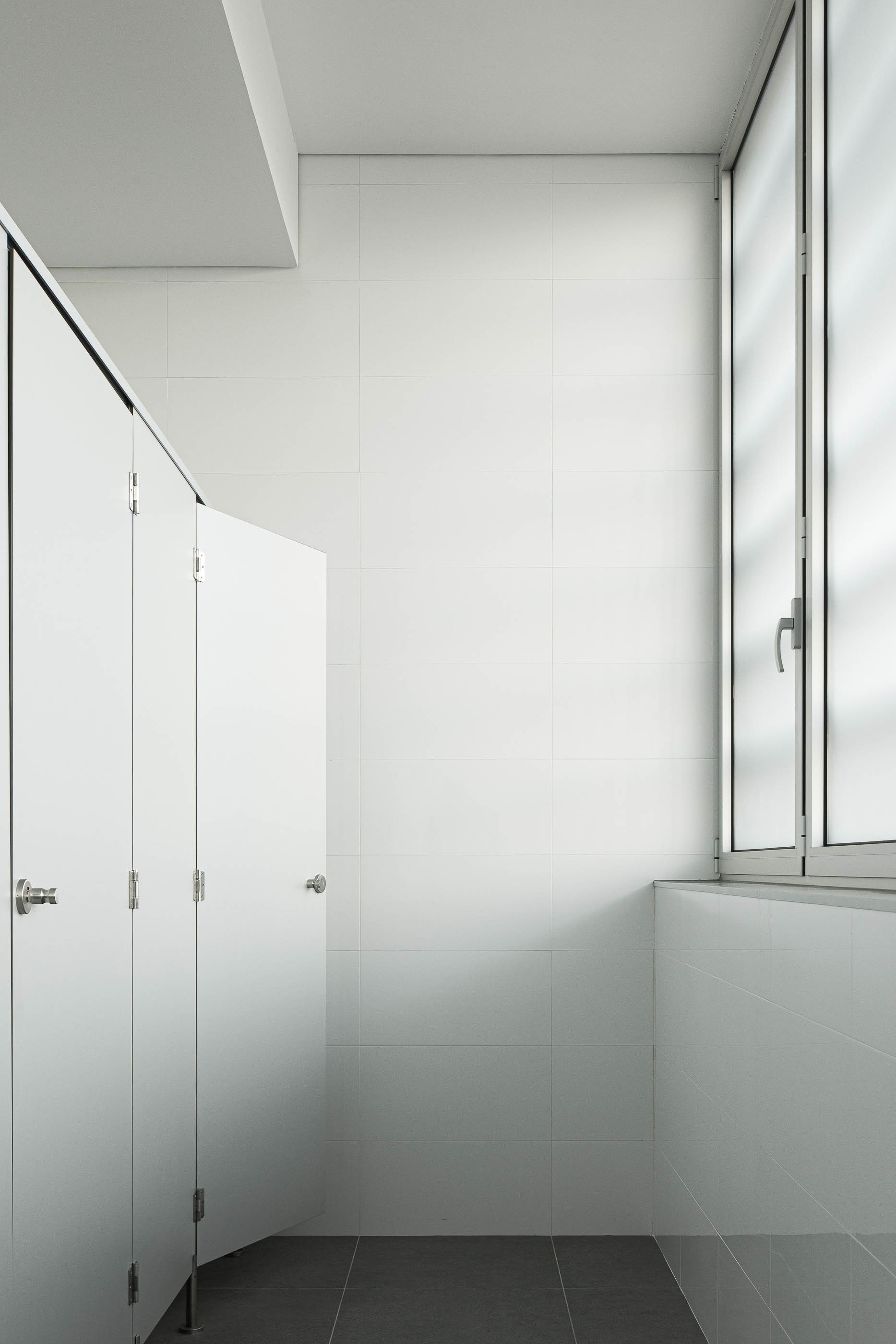 Casa de banho: Cabines sanitárias com portas brancas e revestimento cerâmico branco nas paredes. — Unidade Industrial OROPOL arquitetura Em Paralelo em Castelo de Paiva