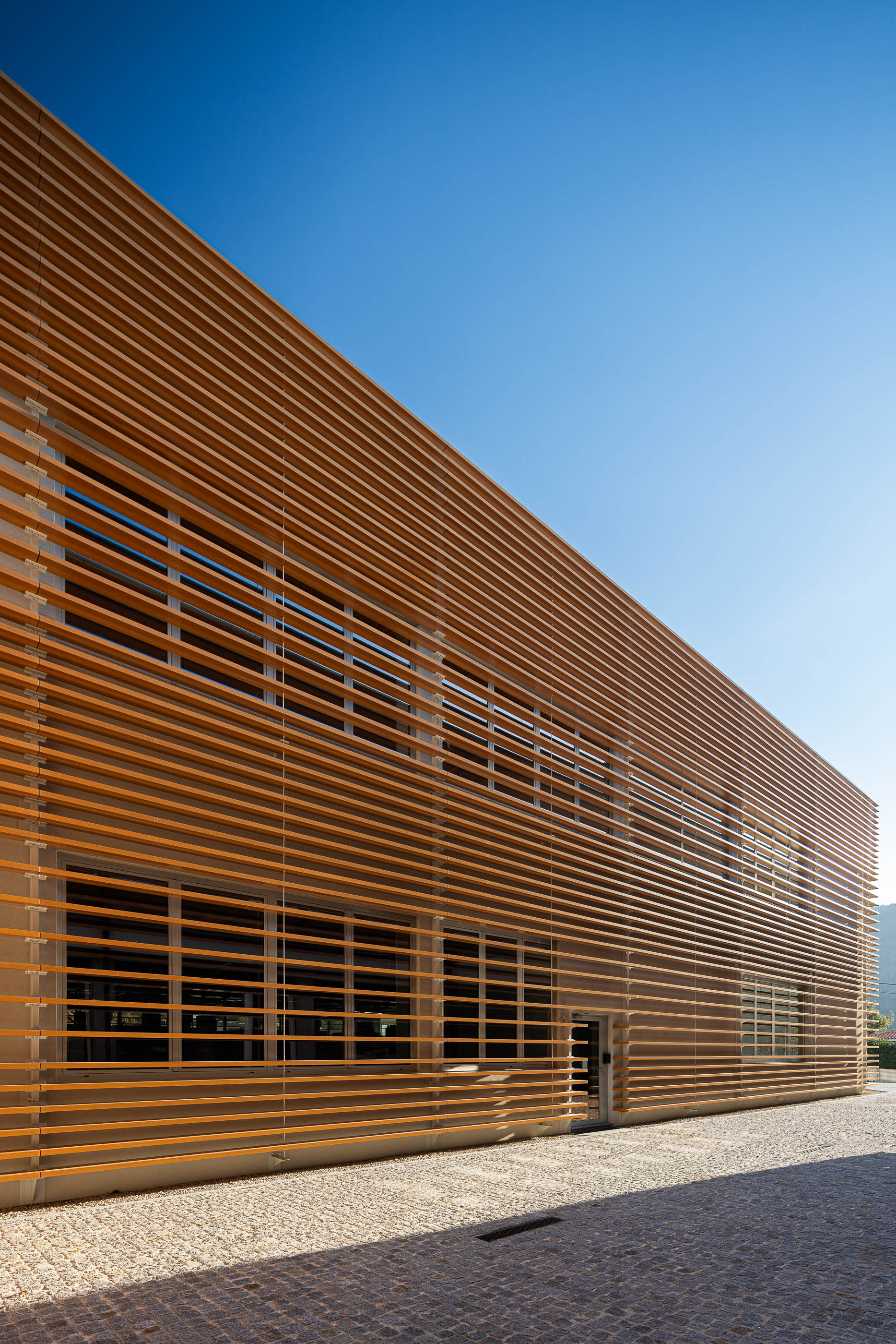 Fachada: Edifício industrial com revestimento em ripas de madeira e porta de acesso. — Unidade Industrial OROPOL arquitetura Em Paralelo em Castelo de Paiva