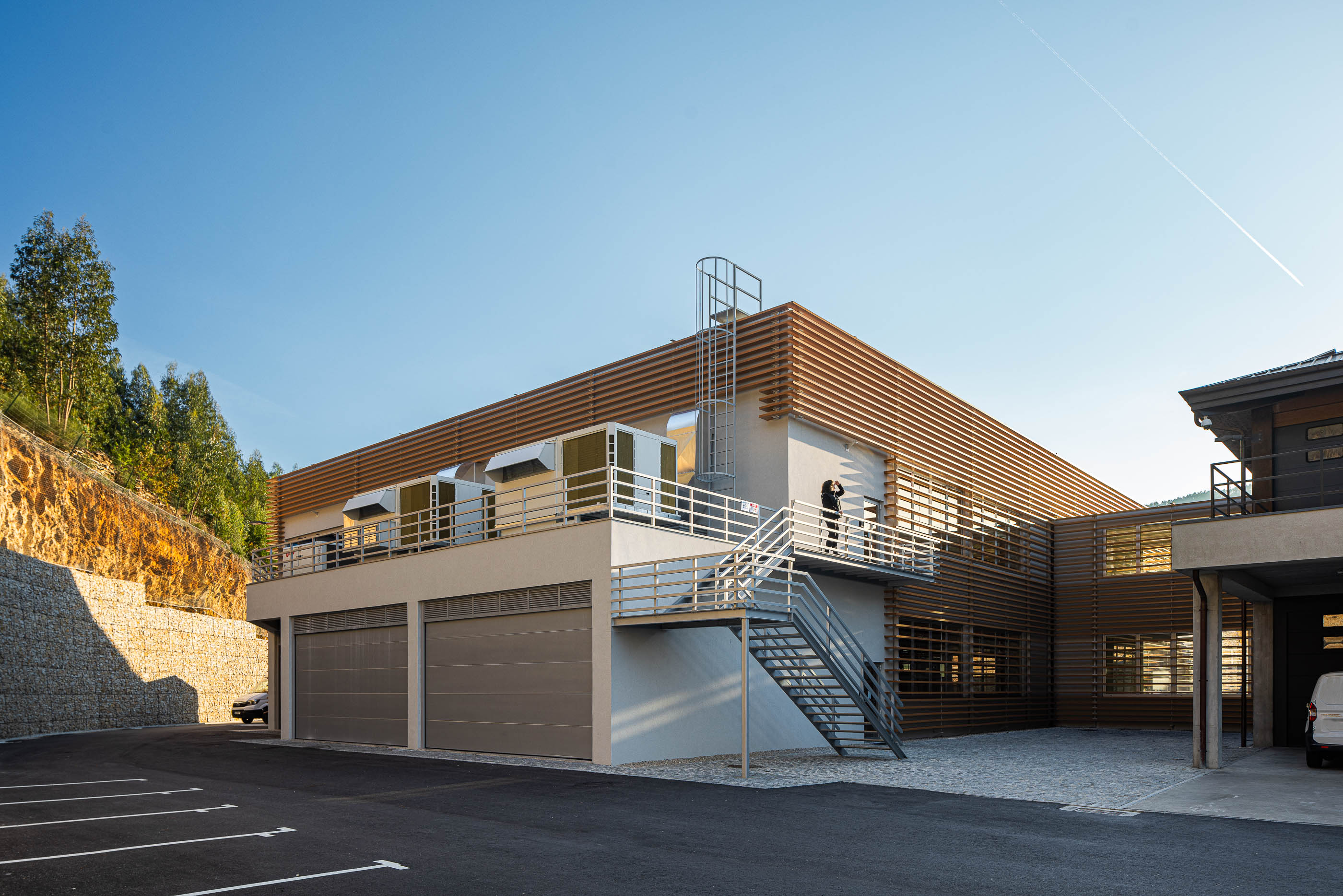 Exterior: Edifício industrial com escadas de acesso ao telhado, garagens e estacionamento. — Unidade Industrial OROPOL arquitetura Em Paralelo em Castelo de Paiva