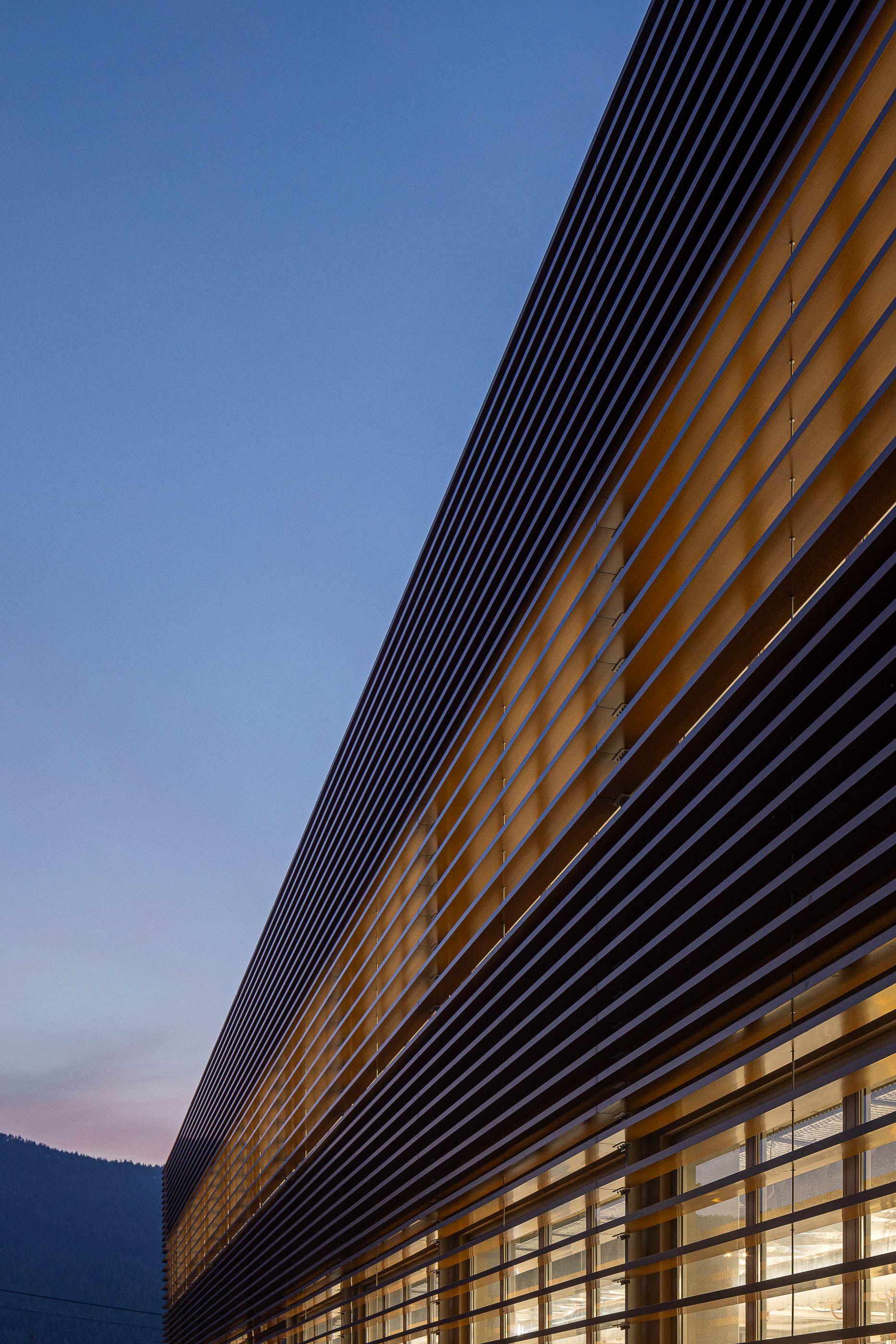 Fachada: Detalhe da fachada com ripas de madeira ao anoitecer. — Unidade Industrial OROPOL arquitetura Em Paralelo em Castelo de Paiva