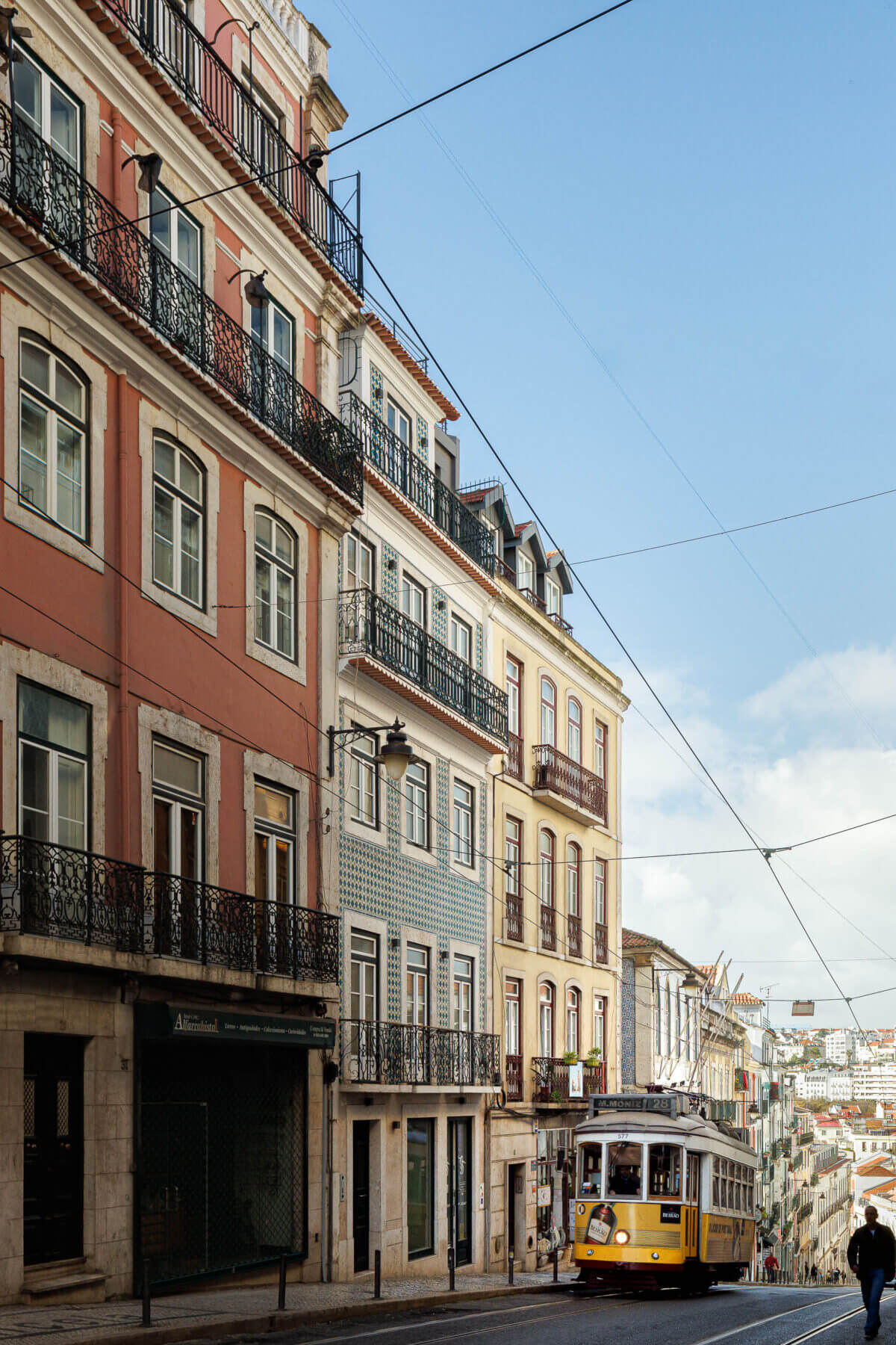 Fachada: Edifício histórico em Lisboa com fachada em tons pastel, varandas em ferro forjado e um elétrico amarelo a passar. — Villa Chiado arquitetura Pedro Carrilho Arquitectos em Lisboa