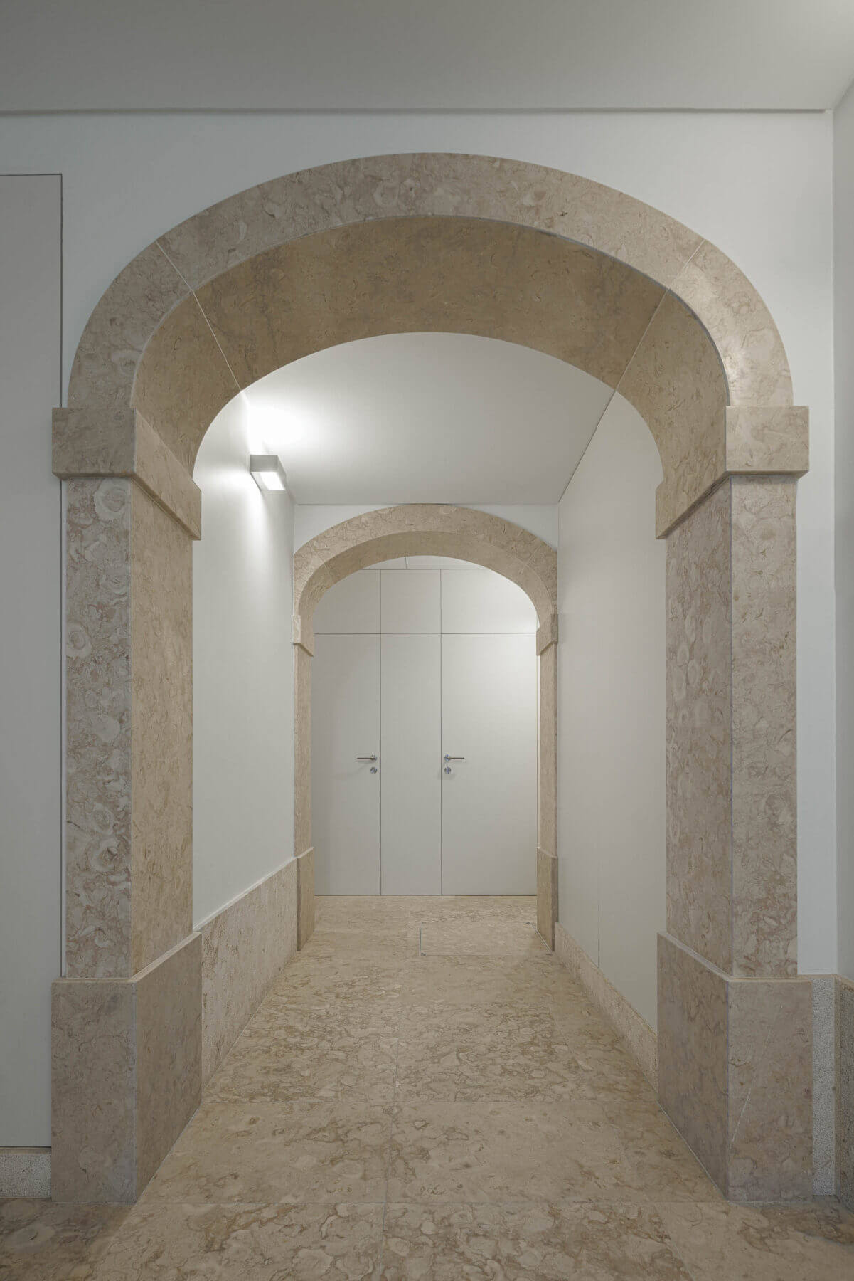 Corredor: Corredor com arcos de pedra, pavimento em pedra clara e paredes brancas minimalistas. — Villa Chiado arquitetura Pedro Carrilho Arquitectos em Lisboa
