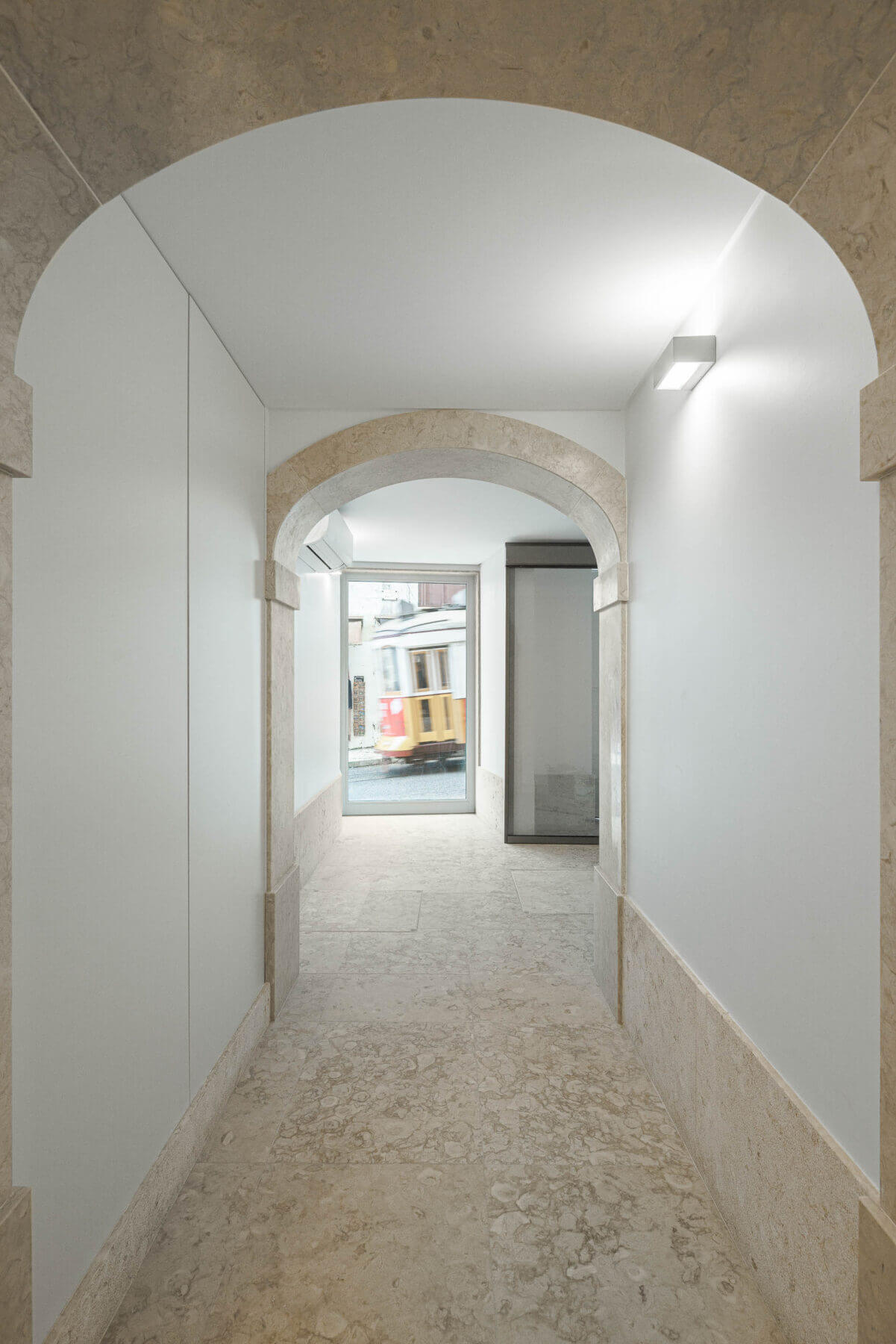 Corredor: Corredor com arcos de pedra, pavimento em pedra clara e vista para a rua com elétrico. — Villa Chiado arquitetura Pedro Carrilho Arquitectos em Lisboa