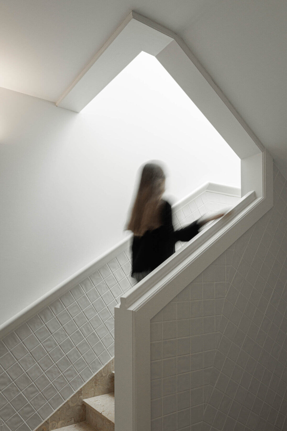 Escadas: Escadas com azulejos brancos e luz natural, pessoa a subir os degraus. — Villa Chiado arquitetura Pedro Carrilho Arquitectos em Lisboa