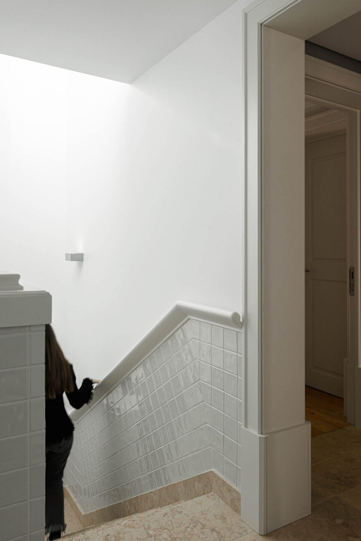 Escadas: Escadas com azulejos brancos, degraus em pedra e porta de acesso ao andar. — Villa Chiado arquitetura Pedro Carrilho Arquitectos em Lisboa