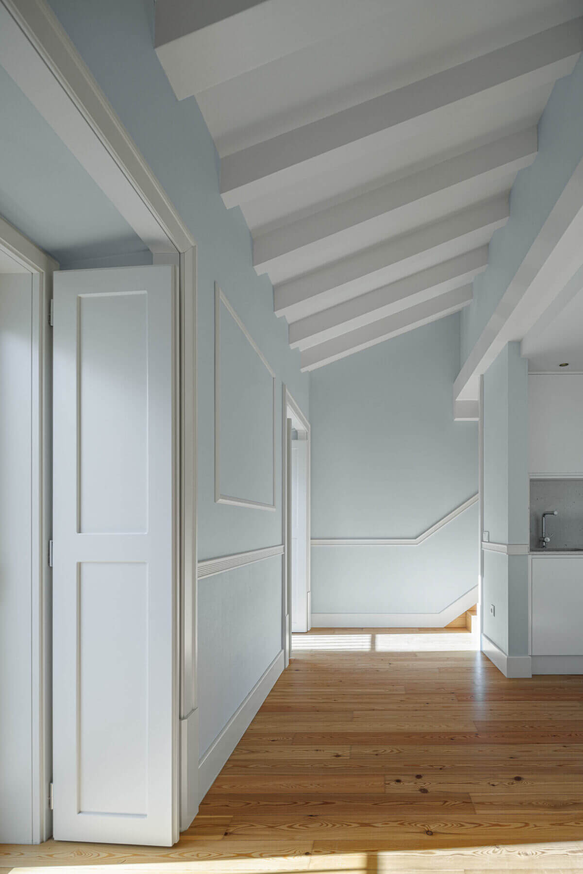 Sótão: Sótão com paredes azul claro, pavimento em madeira e teto com vigas brancas aparentes. — Villa Chiado arquitetura Pedro Carrilho Arquitectos em Lisboa