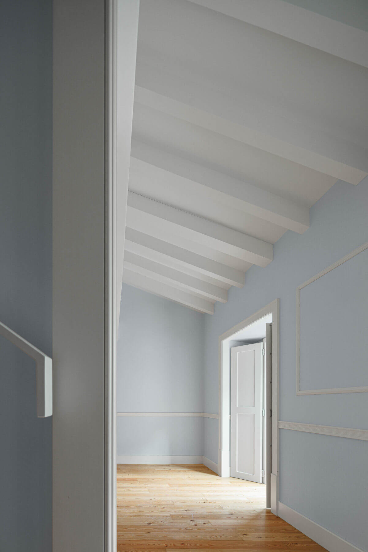 Sótão: Sótão com paredes azul claro, pavimento em madeira e teto com vigas brancas. — Villa Chiado arquitetura Pedro Carrilho Arquitectos em Lisboa