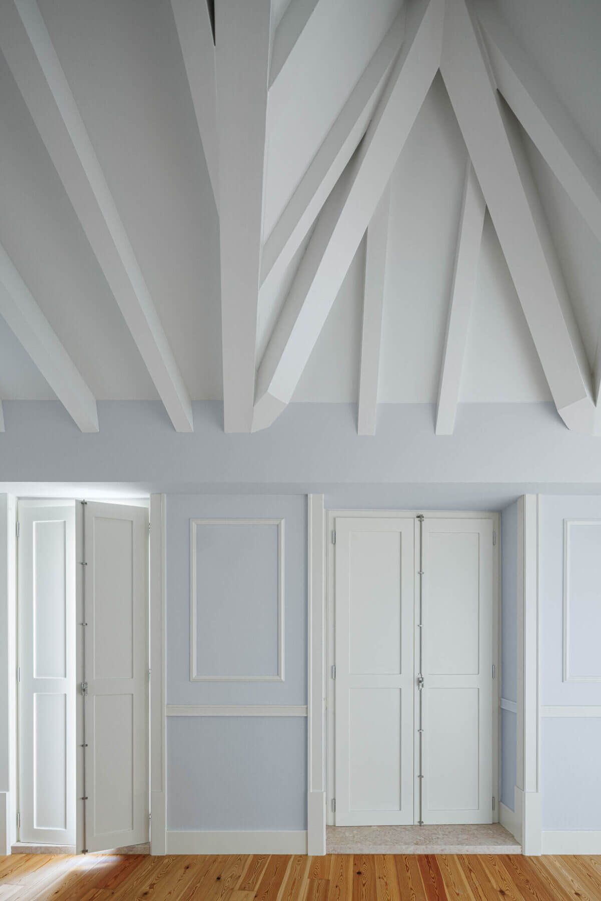 Sótão: Detalhe de paredes azul claro, pavimento em madeira e teto com vigas brancas. — Villa Chiado arquitetura Pedro Carrilho Arquitectos em Lisboa