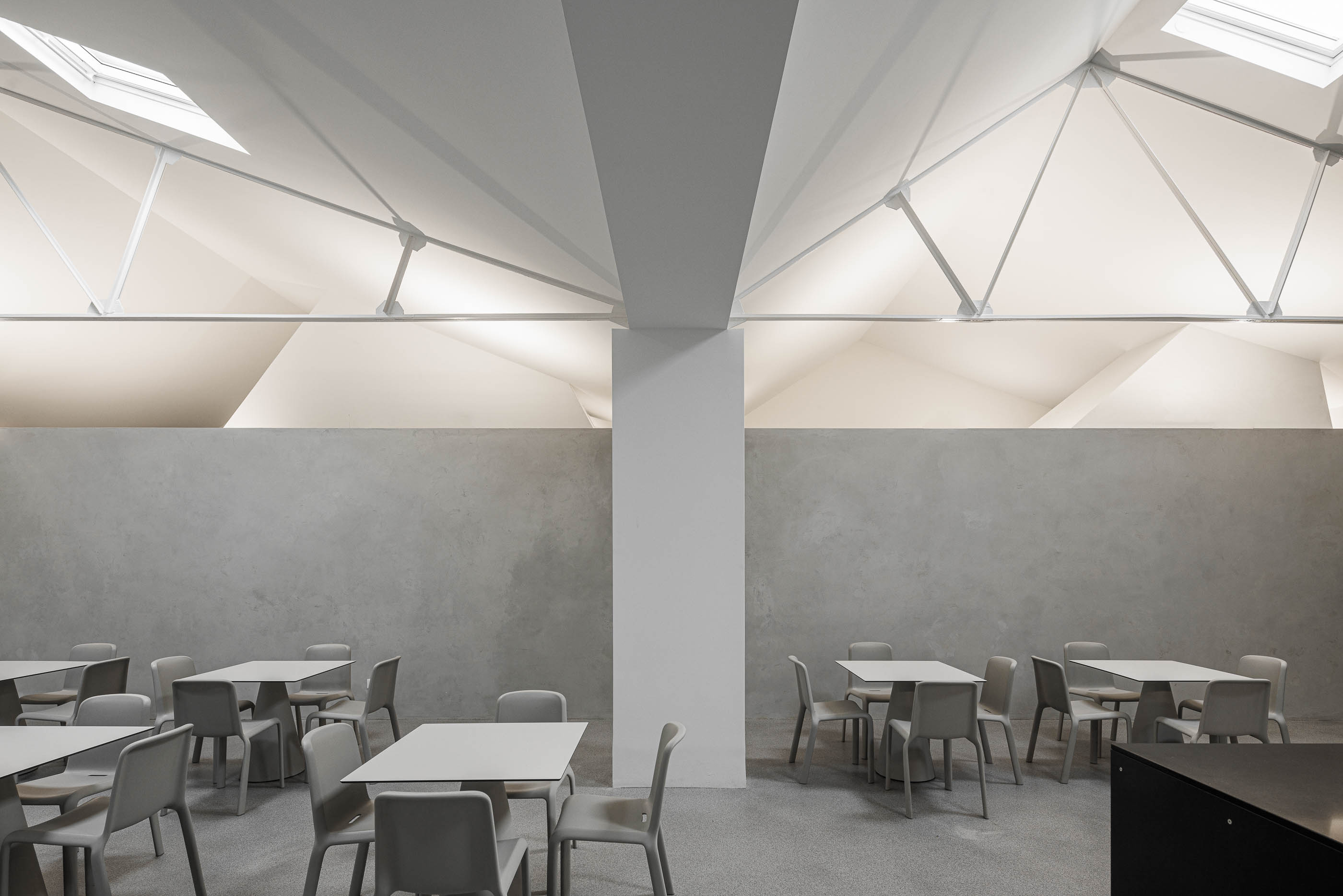 Refeitório: Espaço amplo com mesas e cadeiras cinzentas, iluminado por claraboias e estrutura metálica aparente no telhado. — Indústria | A10 arquitetura BOX arquitectos em São Miguel