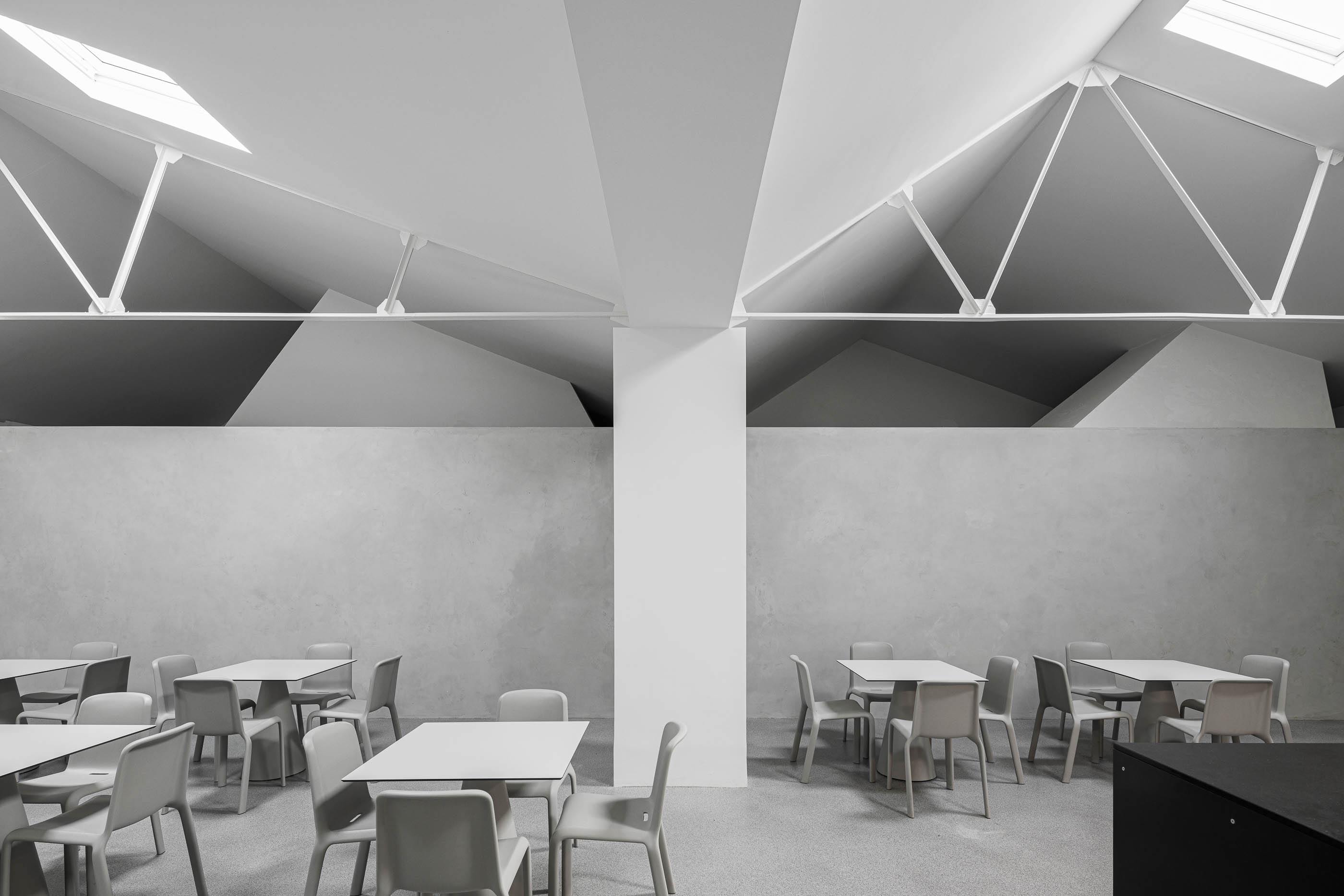 Refeitório: Vista do teto com estrutura metálica branca e claraboias, sobre paredes em cimento afagado e mesas cinzentas. — Indústria | A10 arquitetura BOX arquitectos em São Miguel
