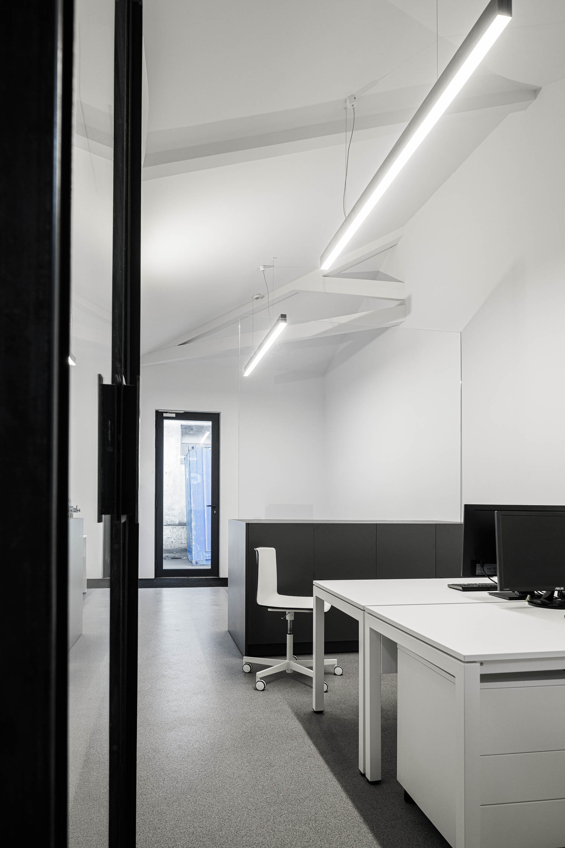 Escritório: Secretária branca com cadeira, balcão cinzento e candeeiros lineares suspensos, pavimento cinzento. — Indústria | A10 arquitetura BOX arquitectos em São Miguel