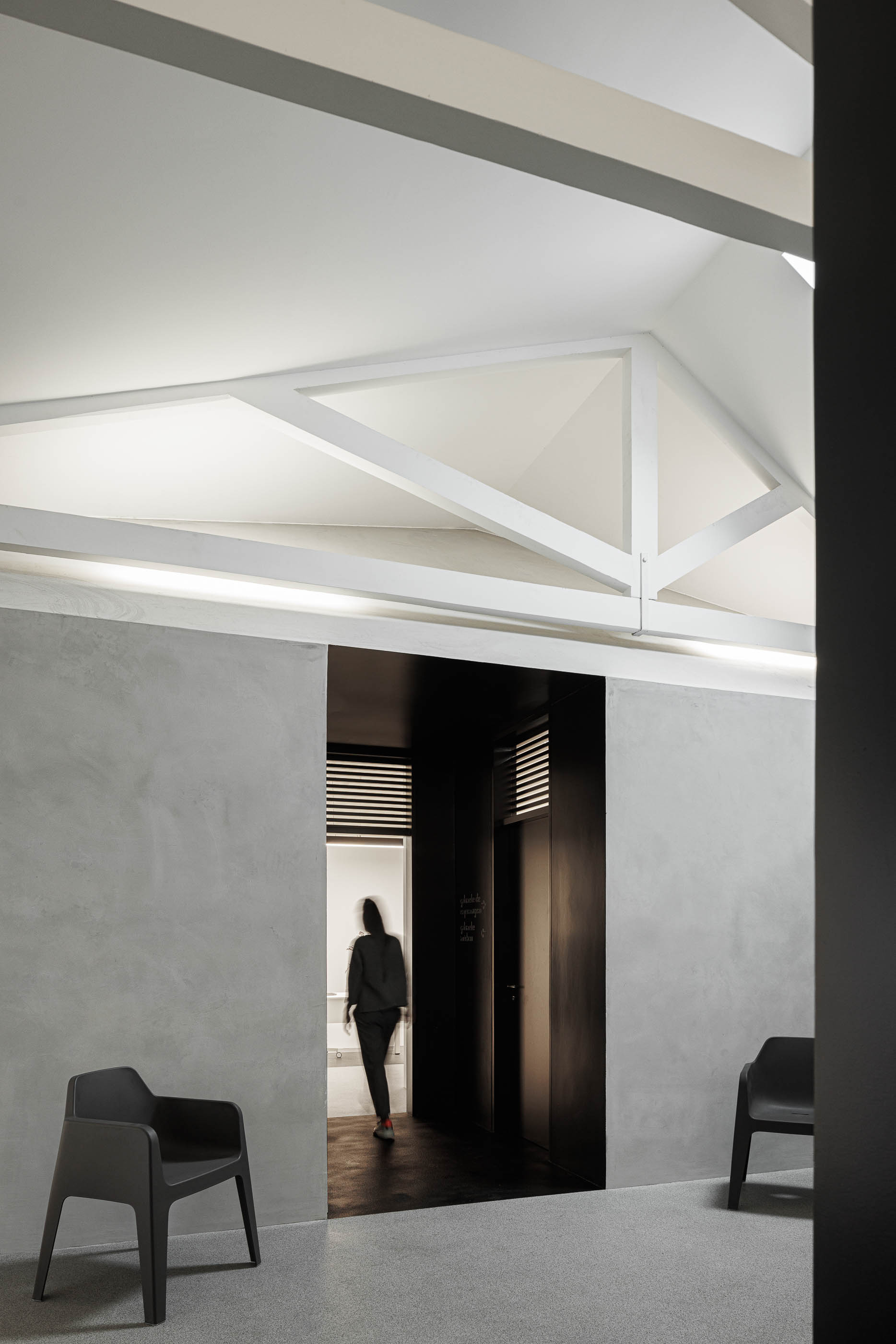 Corredor: Cadeiras cinzentas, paredes em cimento afagado e estrutura branca no teto, com porta preta ao fundo. — Indústria | A10 arquitetura BOX arquitectos em São Miguel