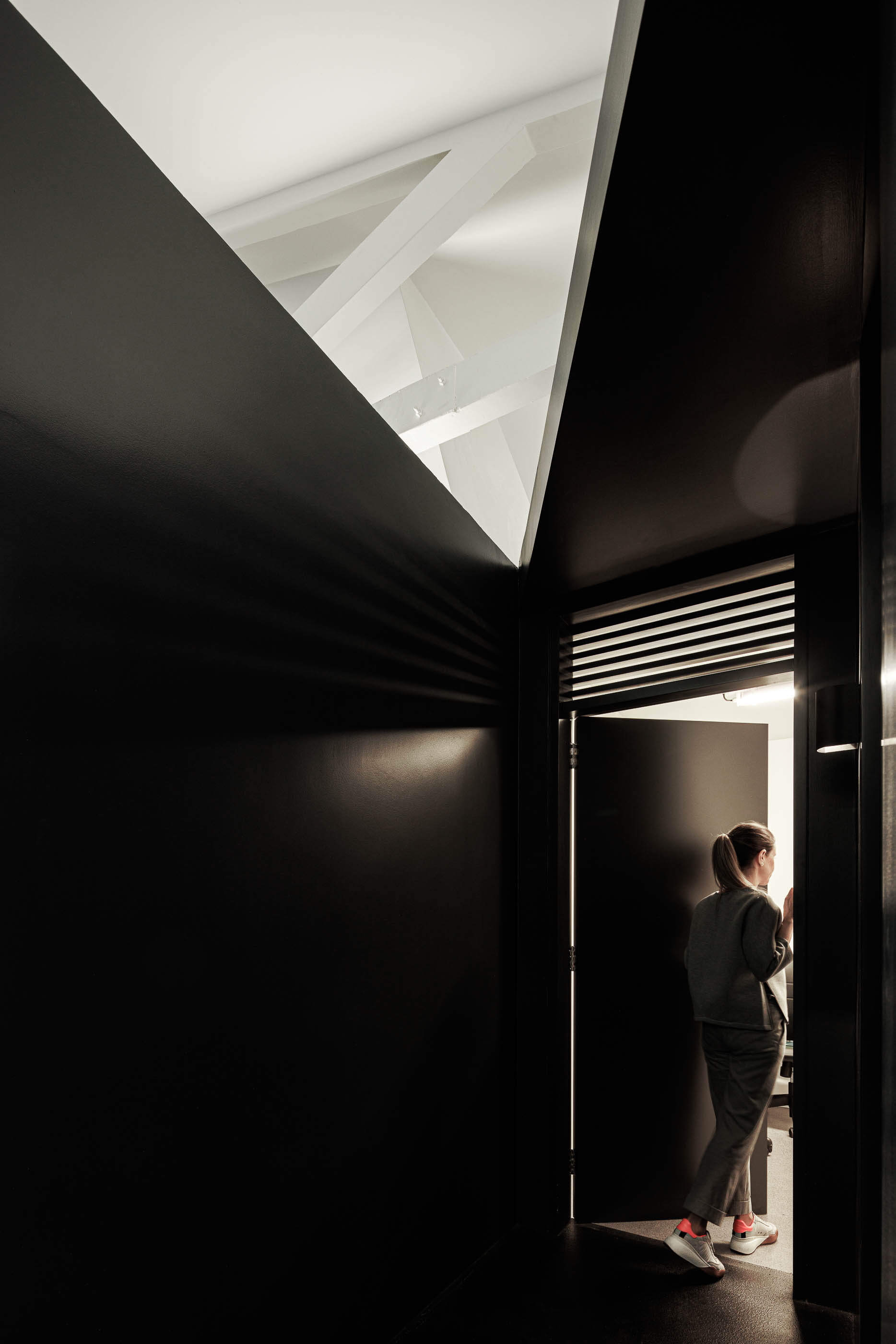 Corredor: Detalhe da porta preta com pessoa a entrar, estrutura branca no teto e parede preta. — Indústria | A10 arquitetura BOX arquitectos em São Miguel