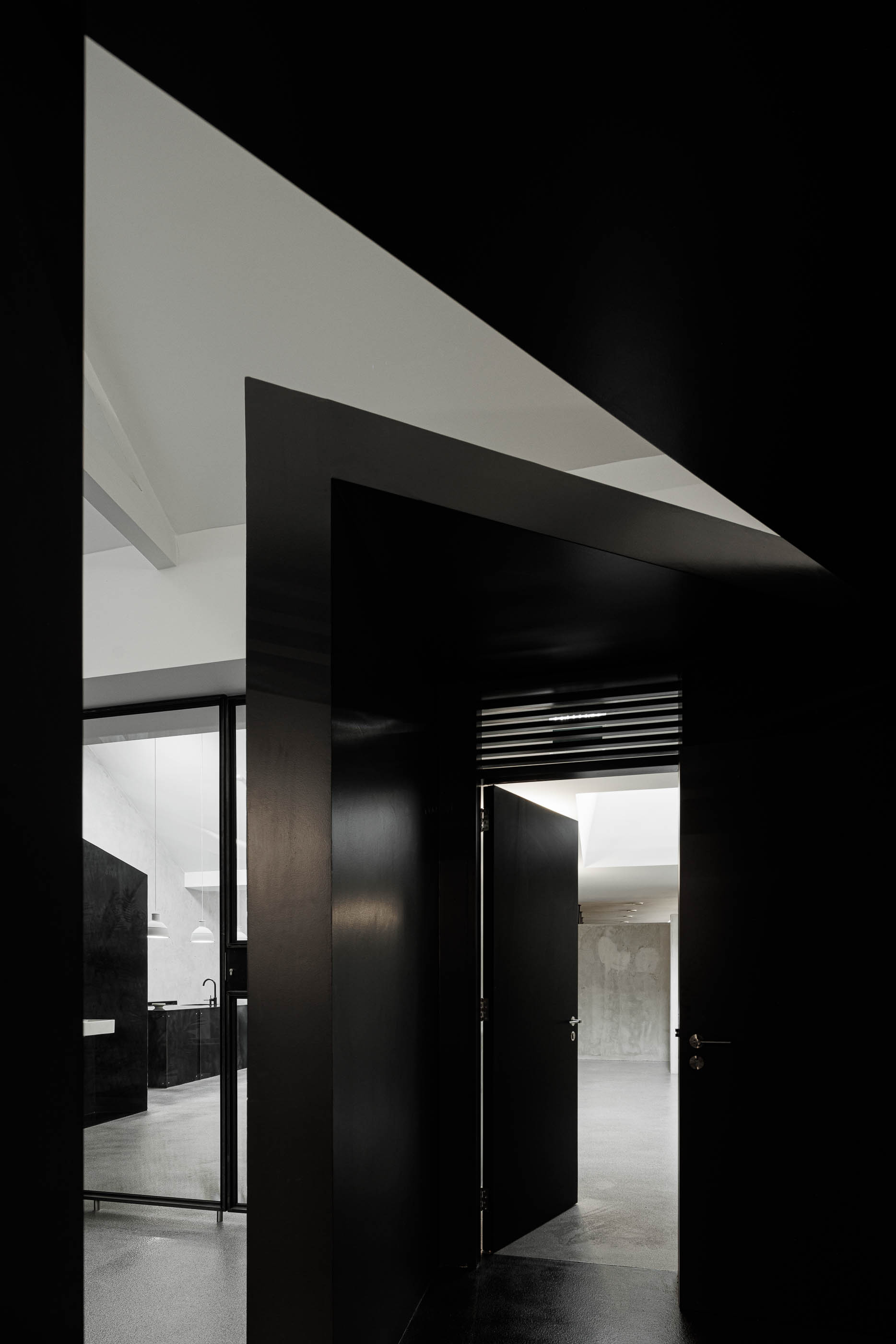 Corredor: Vista através de porta preta para casa de banho com lavatórios brancos e corredor com paredes em cimento afagado. — Indústria | A10 arquitetura BOX arquitectos em São Miguel