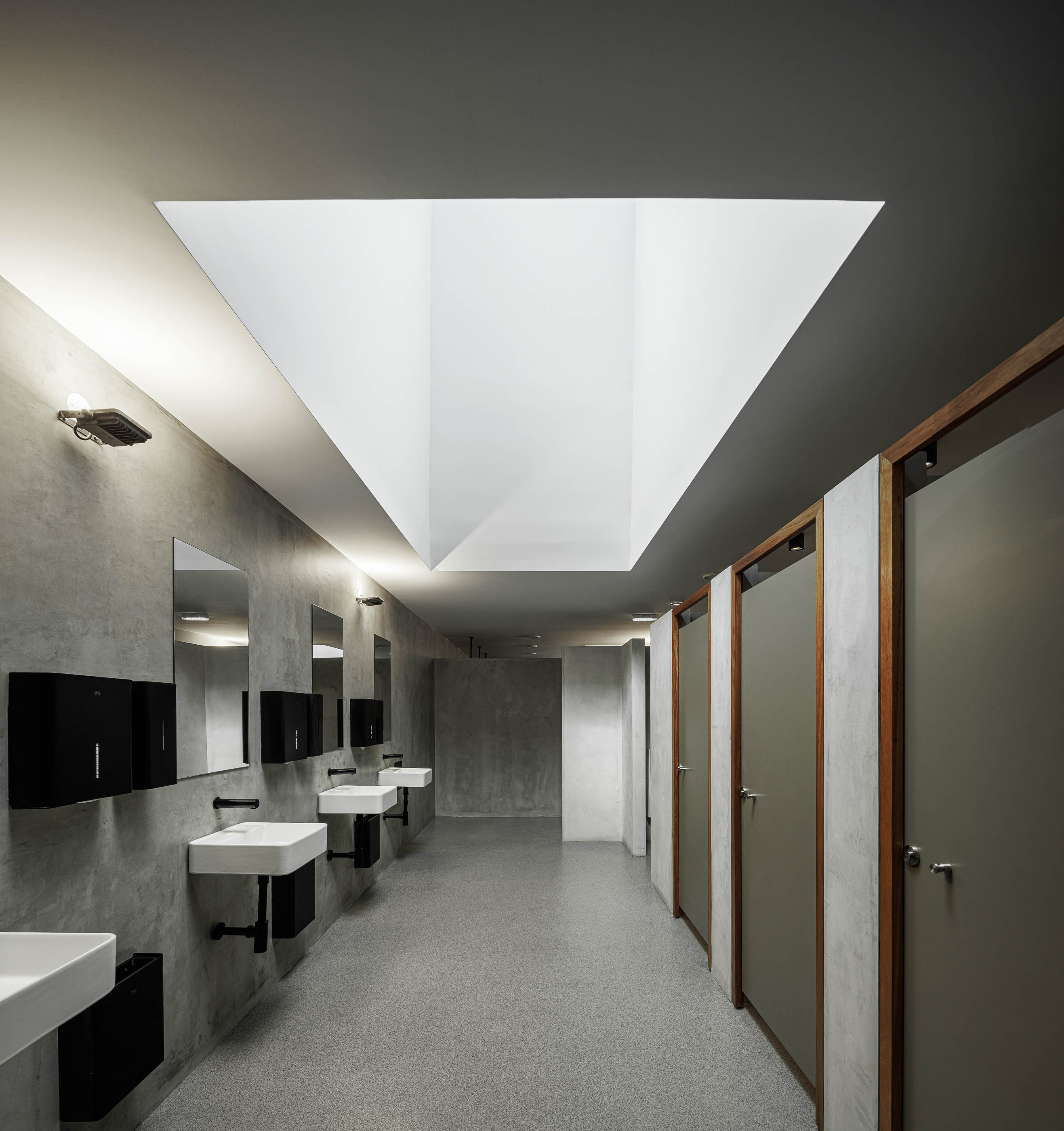 Balneário: Vista geral do balneário com cabines em betão, bancos pretos e claraboias no teto. — Indústria | A10 arquitetura BOX arquitectos em São Miguel